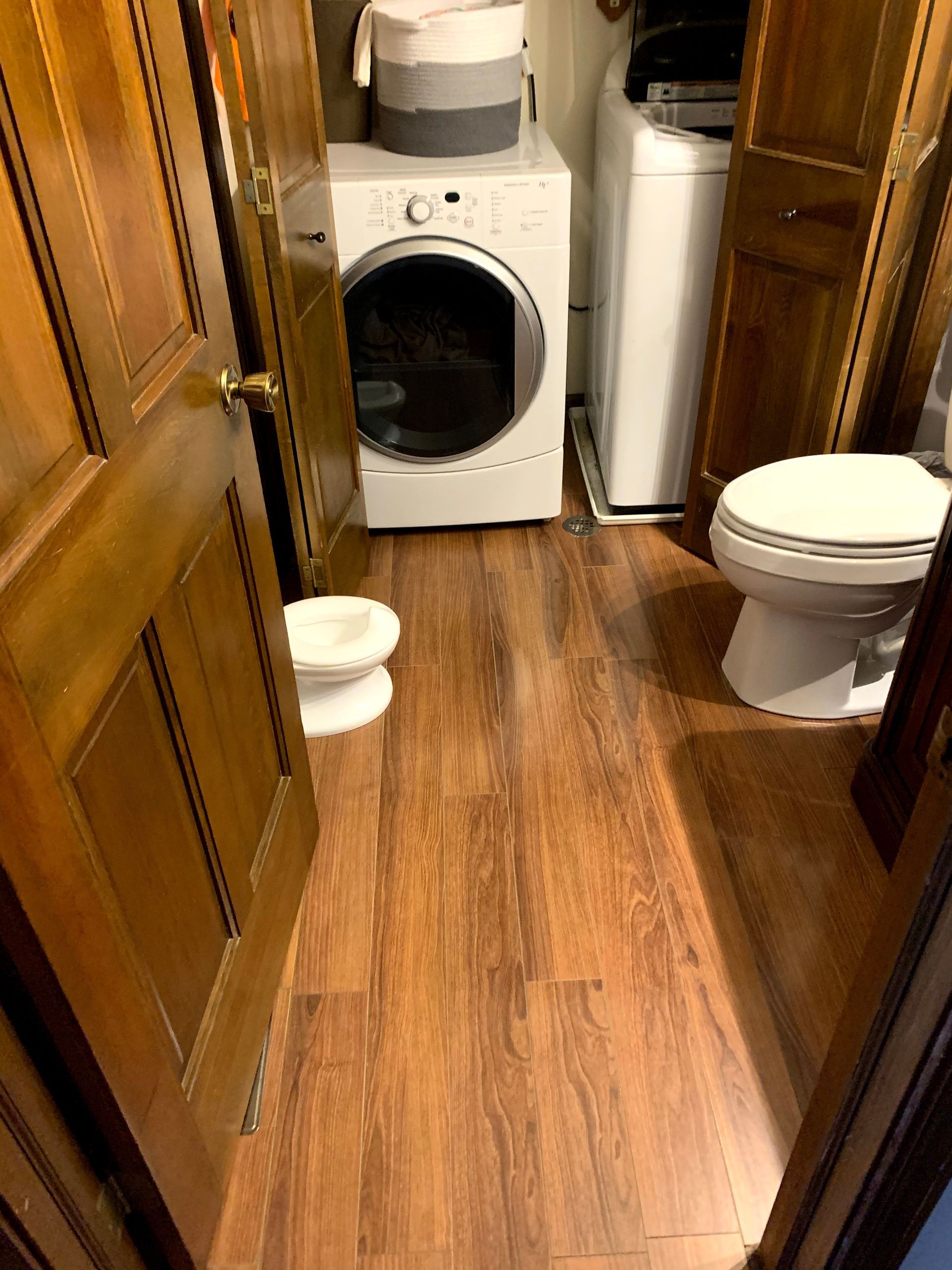 Narrow laundry room with wood cabinets, washer, dryer, toilet, and small pet bowls on the floor.