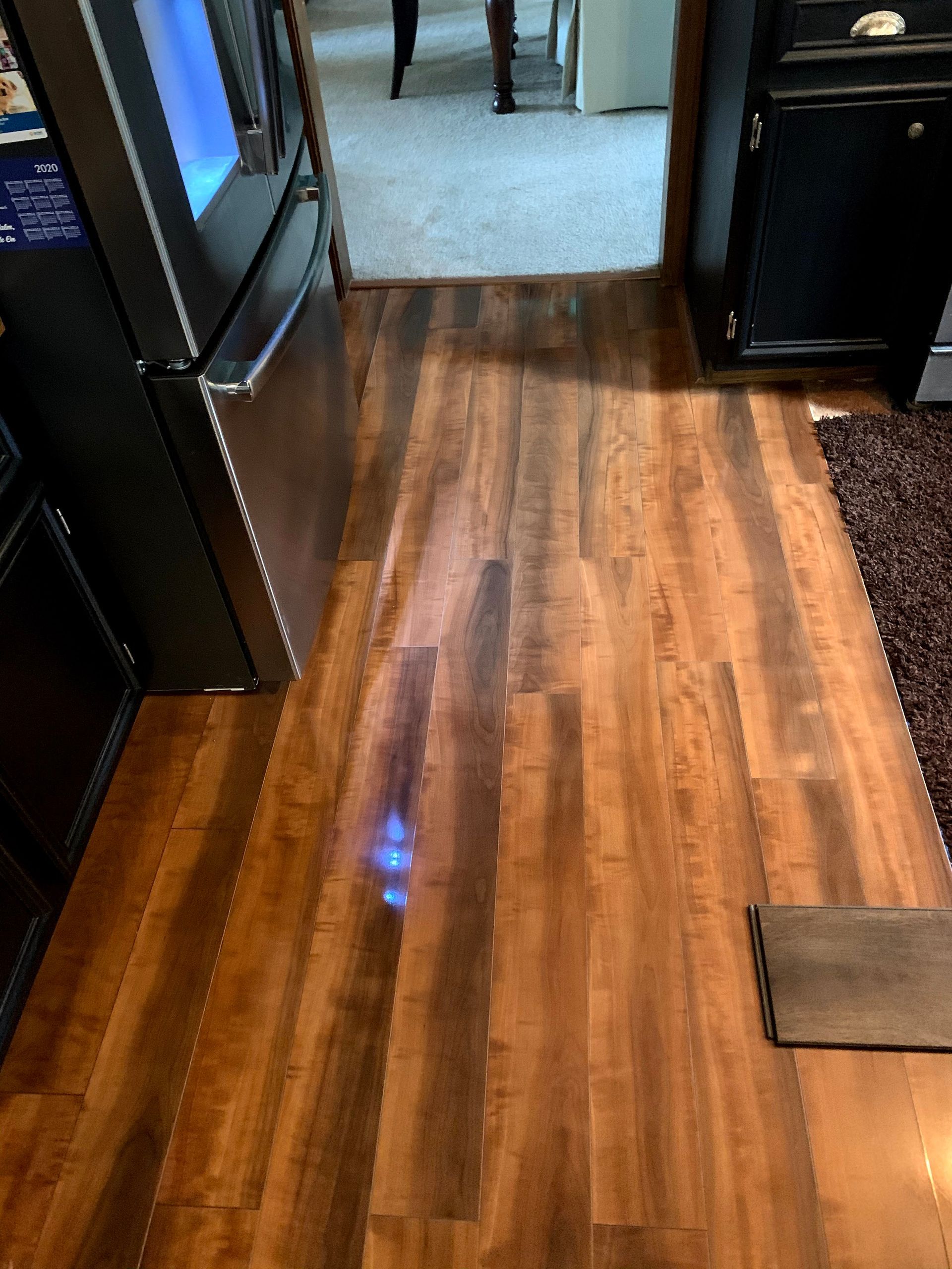 Wooden hallway floor leading to a carpeted room, with dark doorframes on both sides.