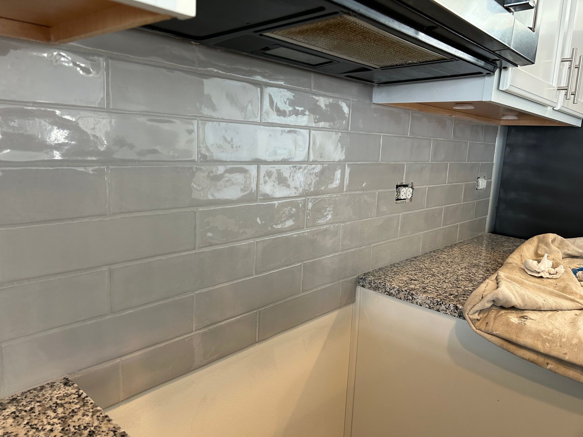 Gray subway tile backsplash under kitchen cabinets with speckled countertop and a bag on the right.