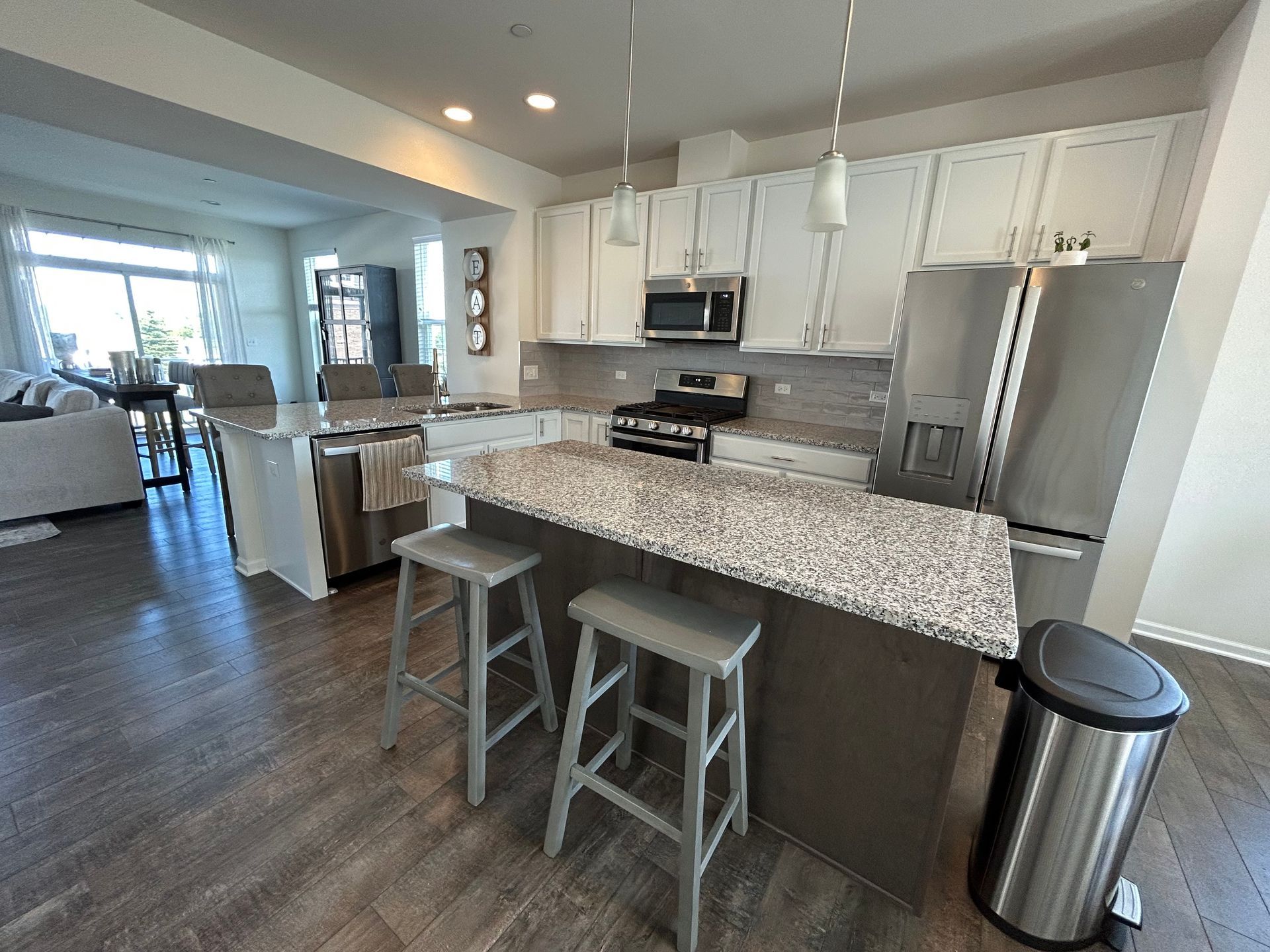 Modern kitchen with granite island, two stools, stainless appliances, and open living area in the background