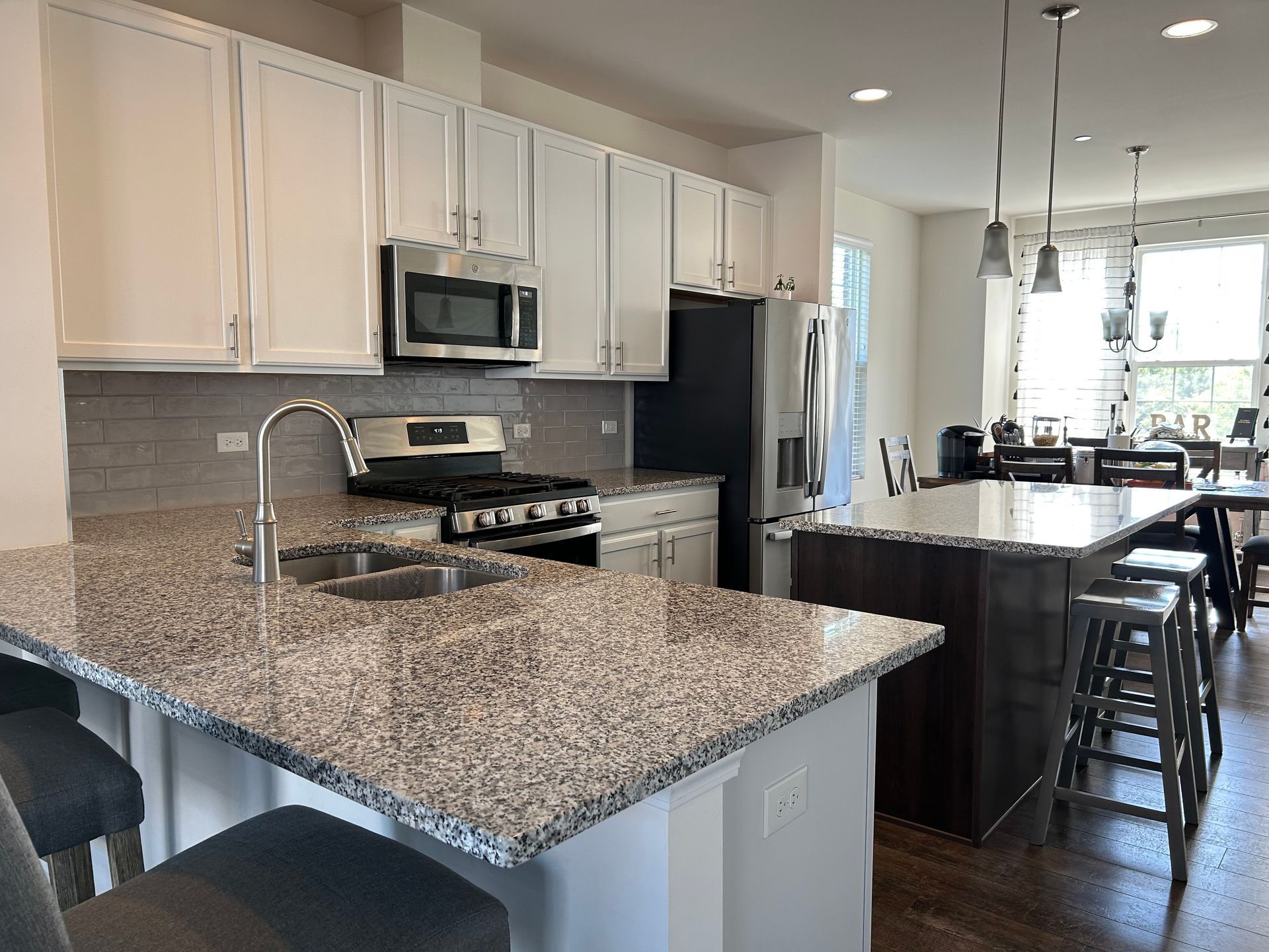 Modern kitchen with granite island, white cabinets, stainless appliances, and a dining area by large windows