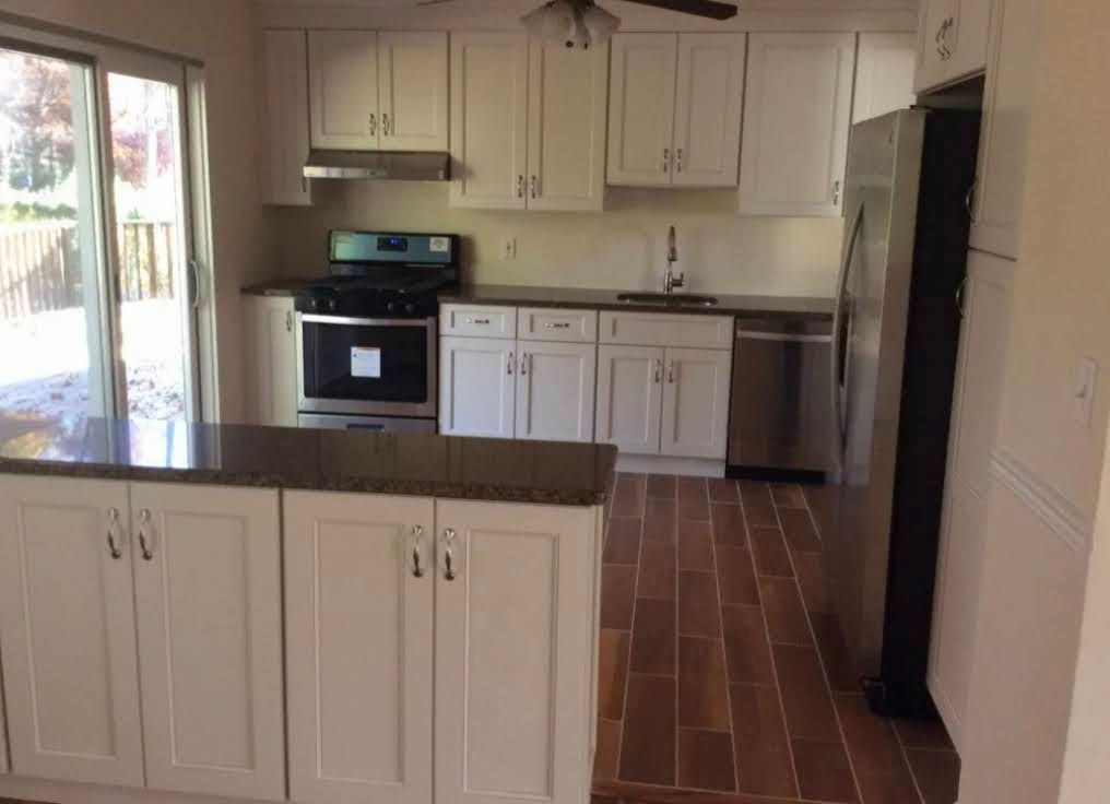 Empty kitchen with white cabinets, black appliances, brown tile floor, and a sliding glass door.