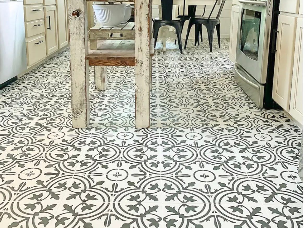 Decorative black-and-white patterned kitchen floor with light cabinets and wooden table legs
