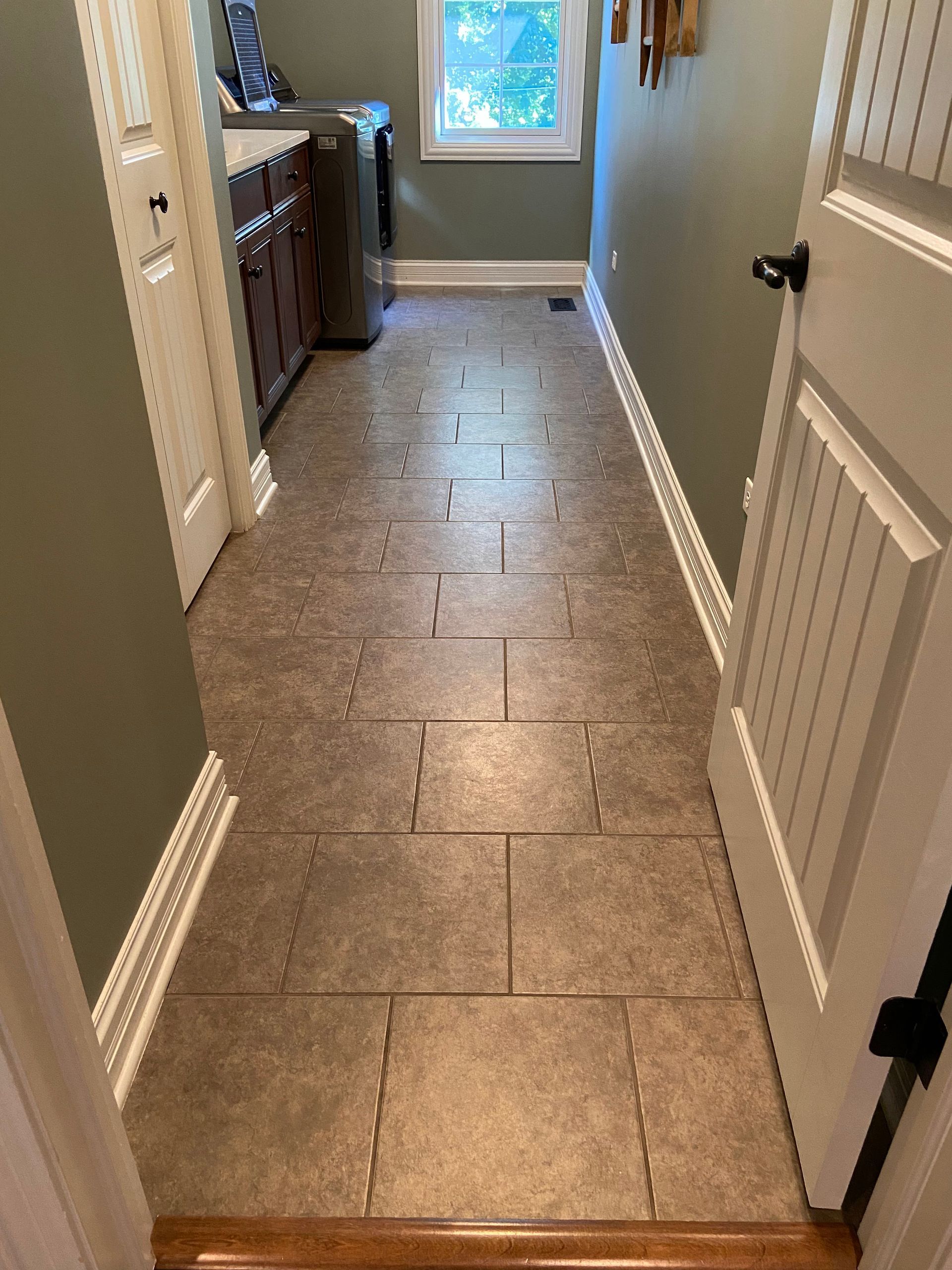Narrow tiled hallway with cabinets on the left and a window at the end.