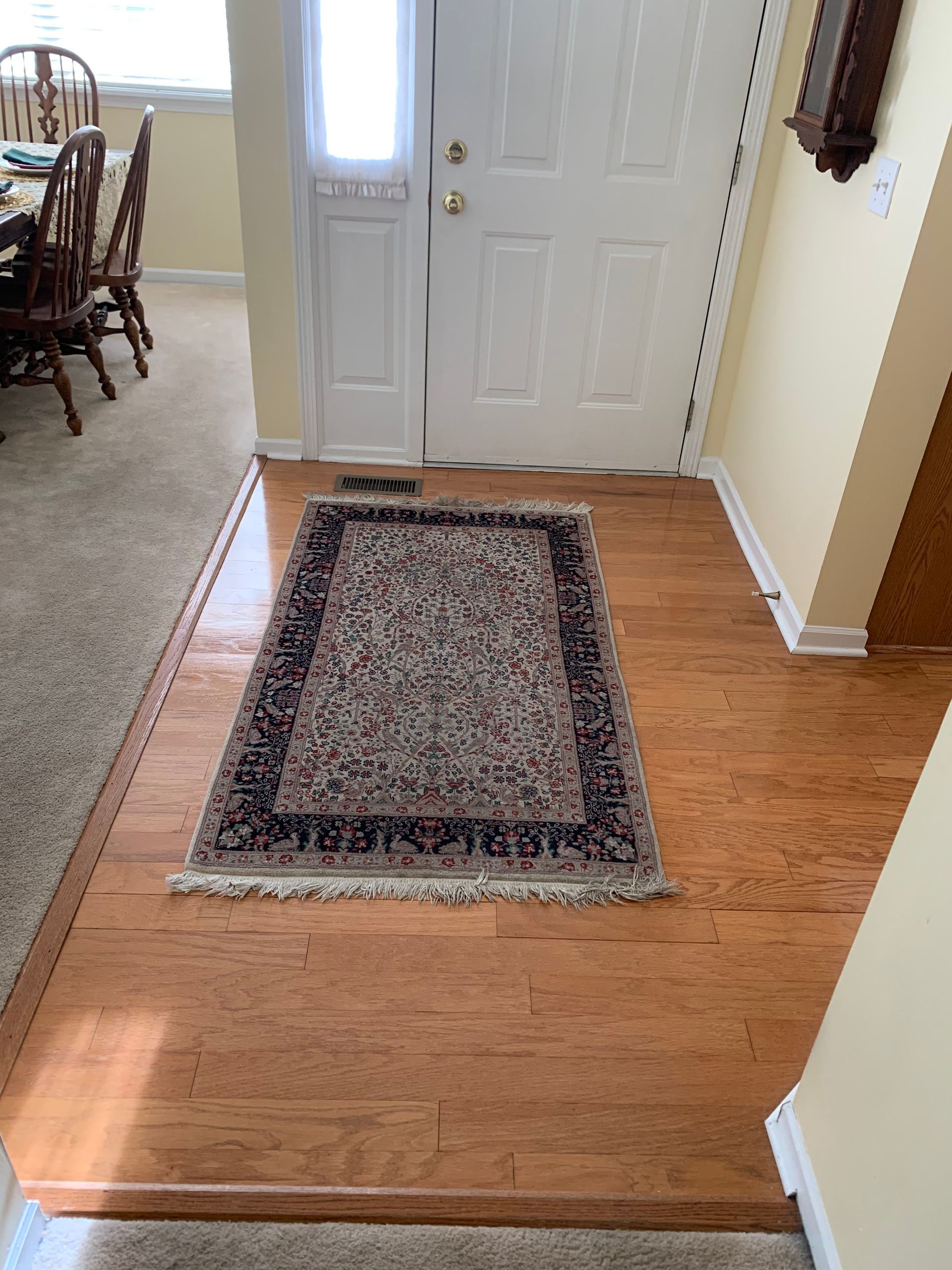 Front entryway with a white door, wood floor, and a patterned rug centered on the landing.