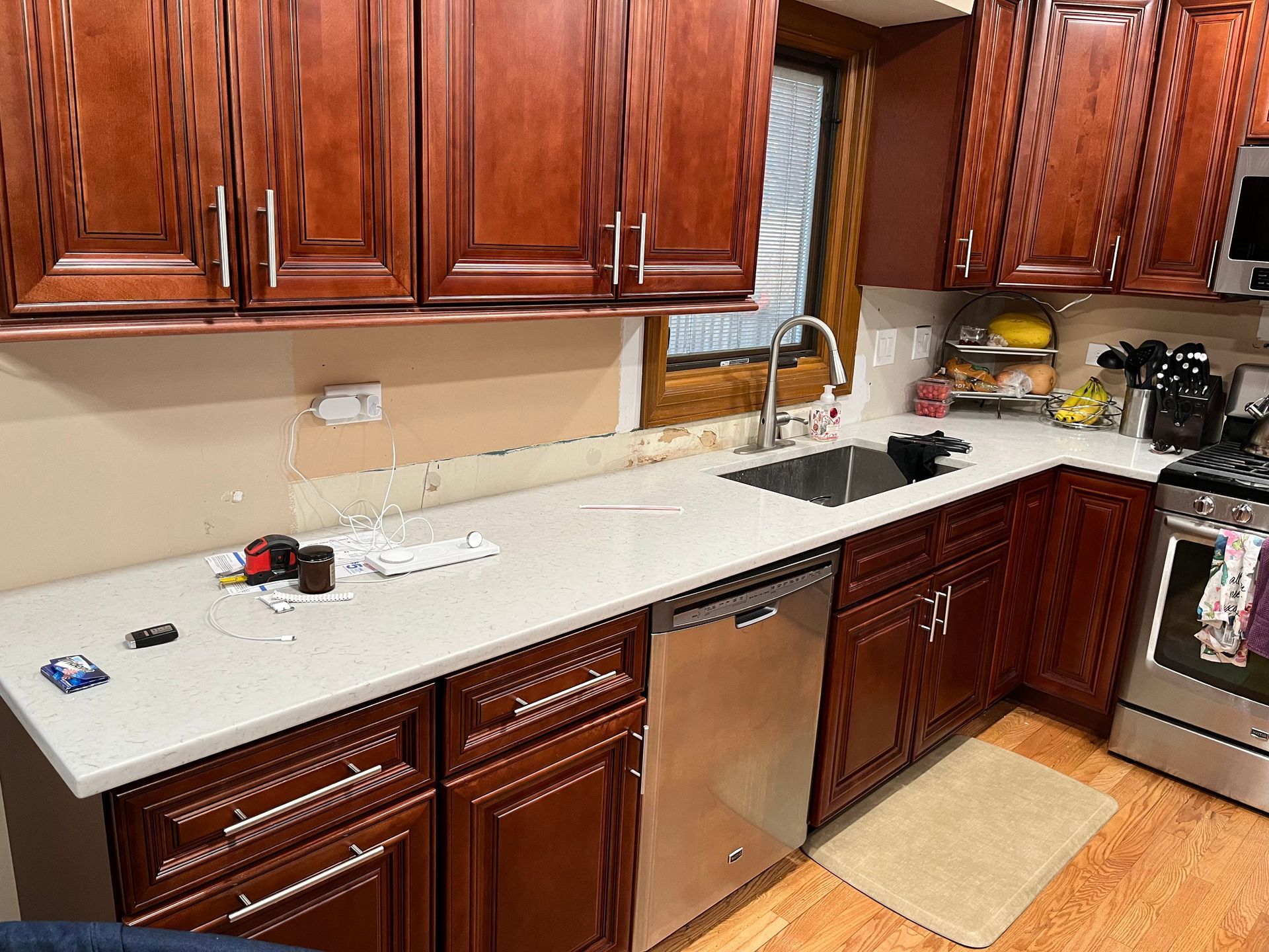 Kitchen with wooden cabinets, white countertop, sink by window, dishwasher, and a beige rug on the floor