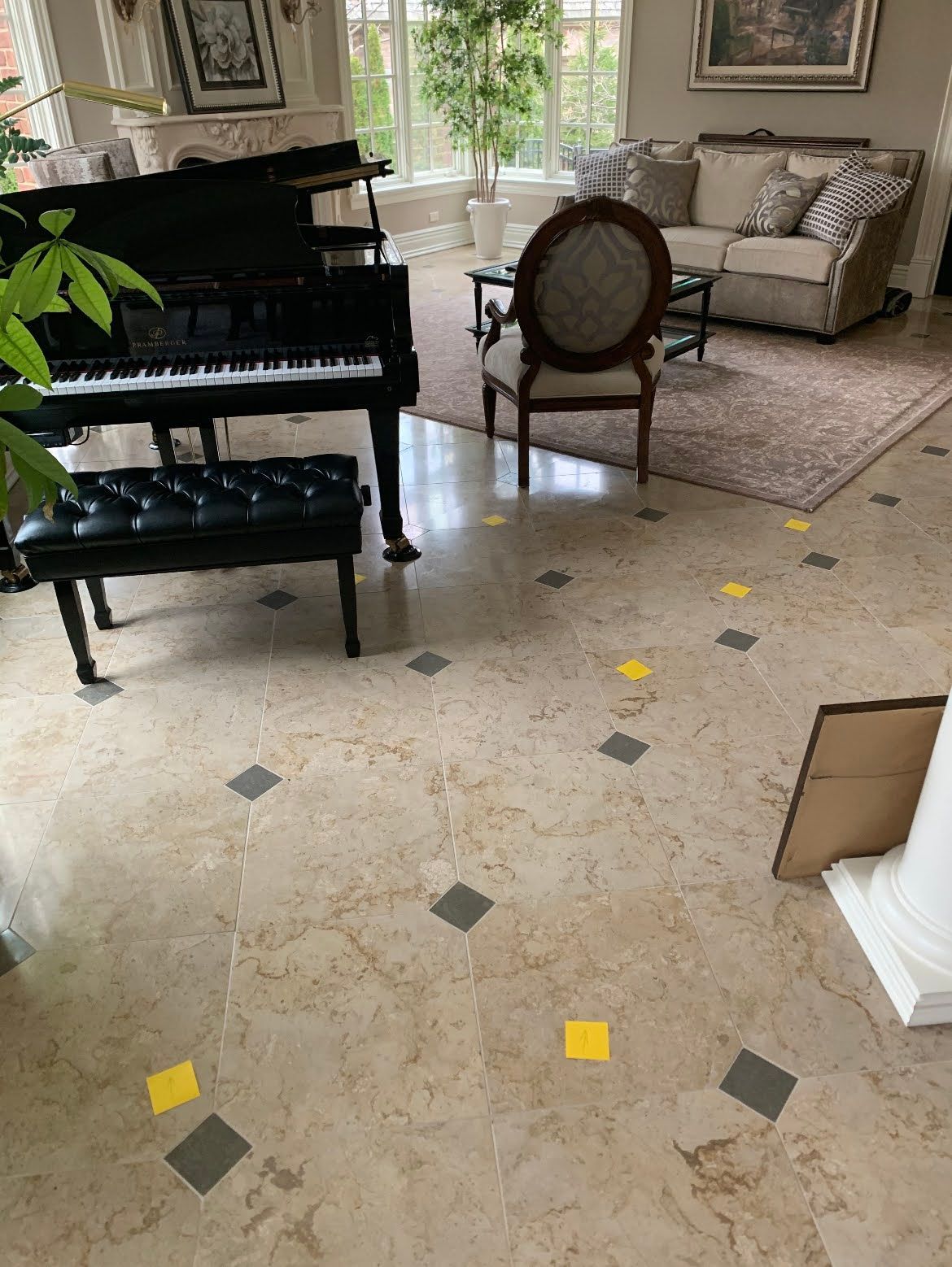 Living room with black grand piano, sofa, chair, and stone floor with yellow markers