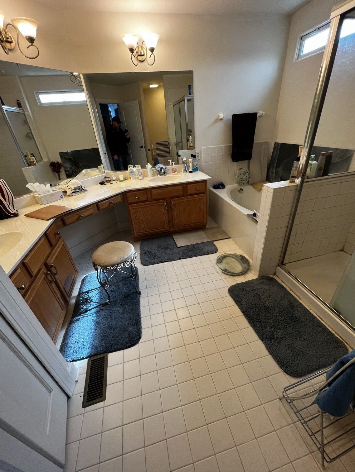 Spacious beige bathroom with double vanity, mirrors, tub, shower, and tiled floor mats