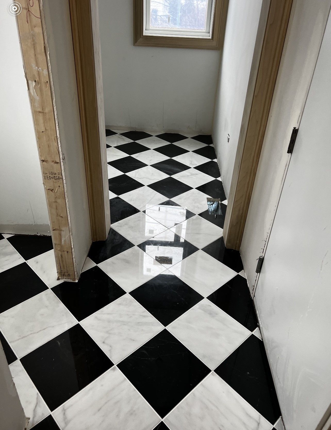 Narrow hallway with black-and-white checkered floor and open doorways leading to a small room.