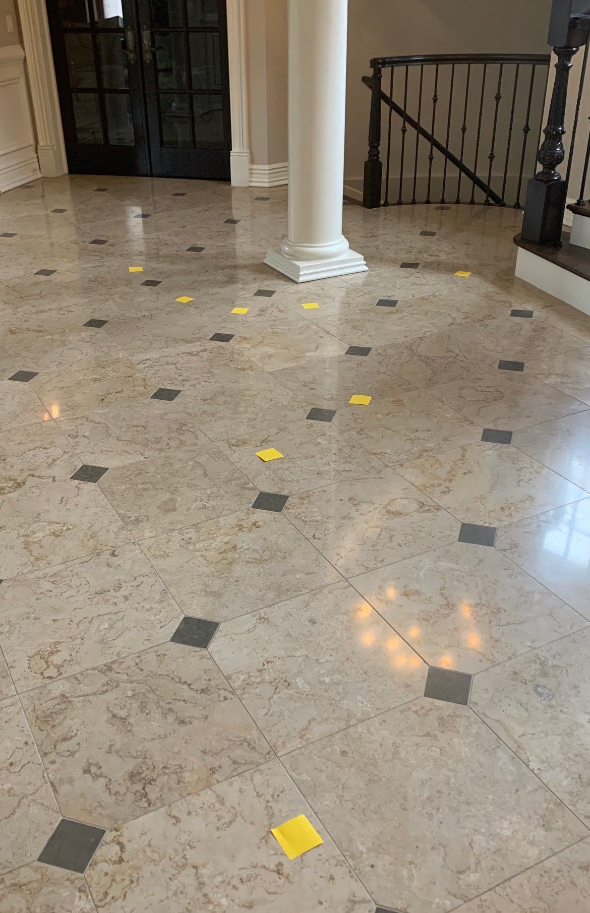 Marble lobby floor with scattered yellow and gray square markers near a white column and stair railing