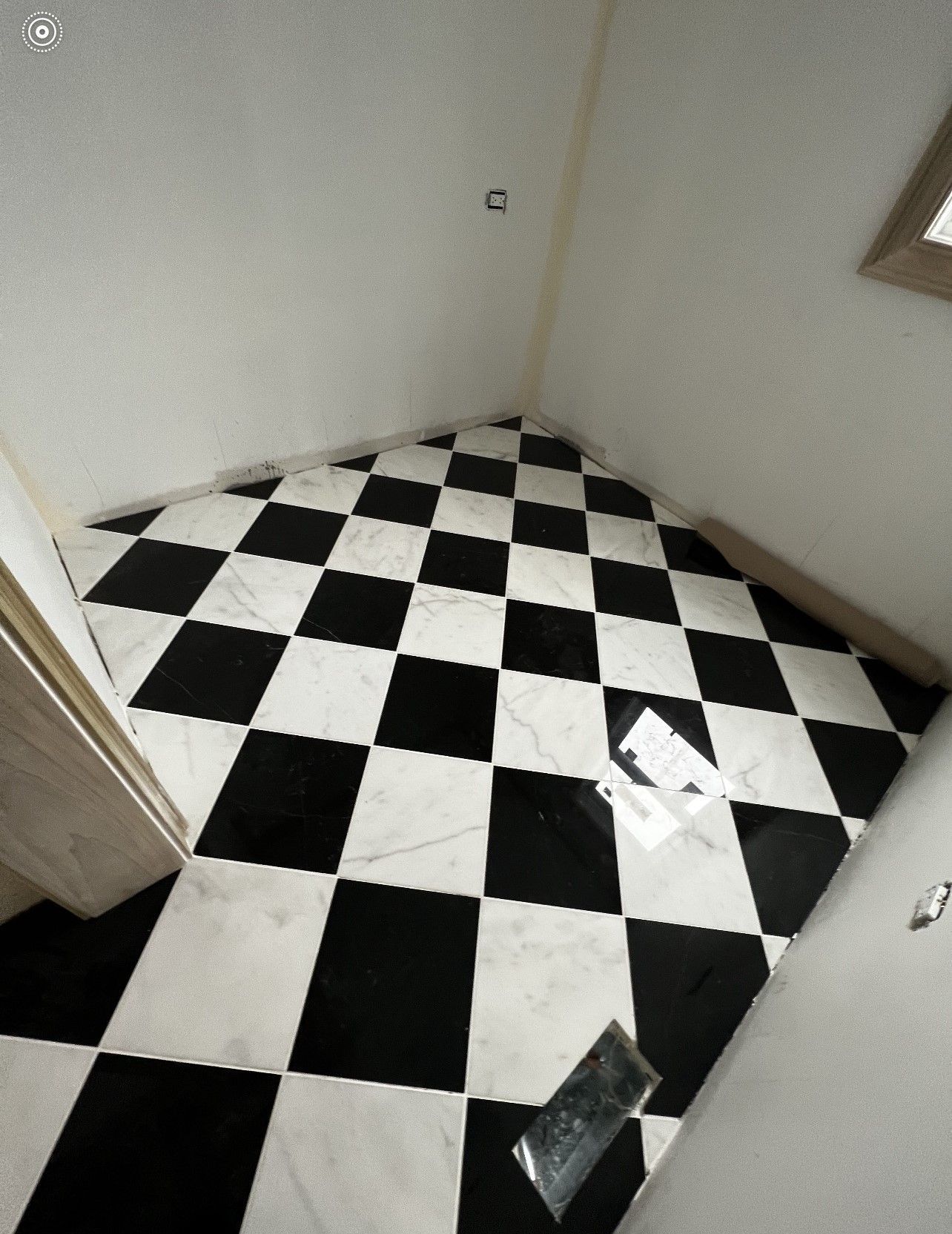 Small empty room with black-and-white checkered tile floor and plain walls, viewed from the doorway