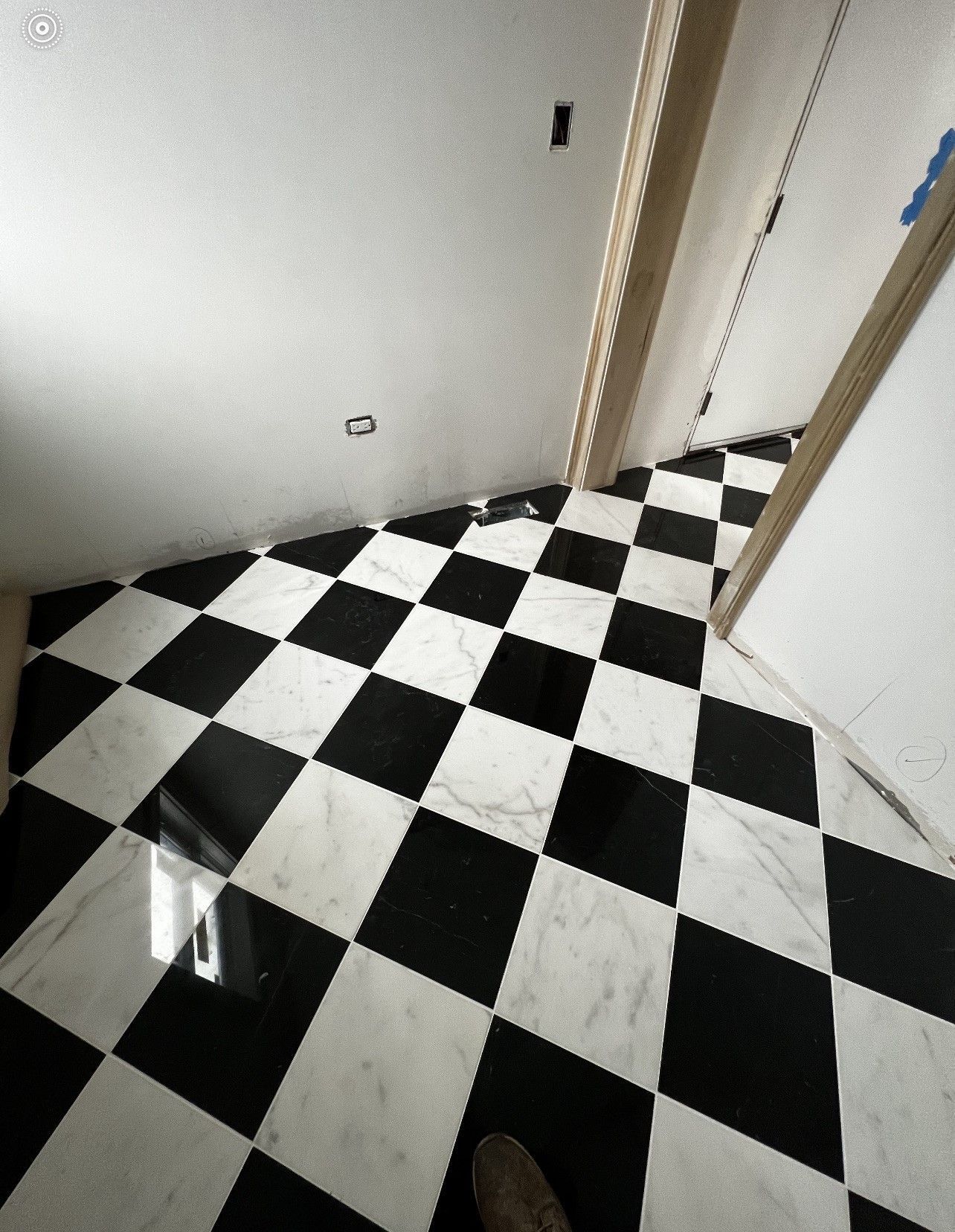 Black-and-white checkered floor in a hallway with white walls and a doorway.