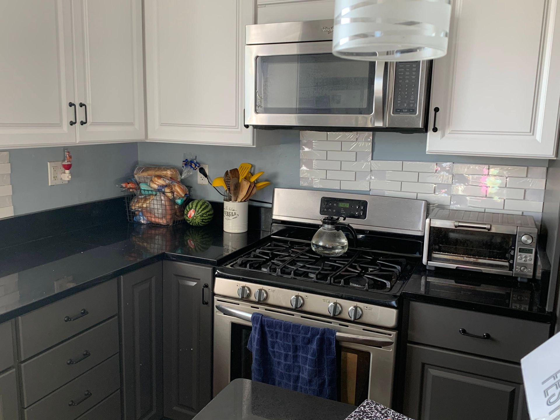 Modern kitchen with white cabinets, stainless steel stove and microwave, black countertops, and a glass pendant light.