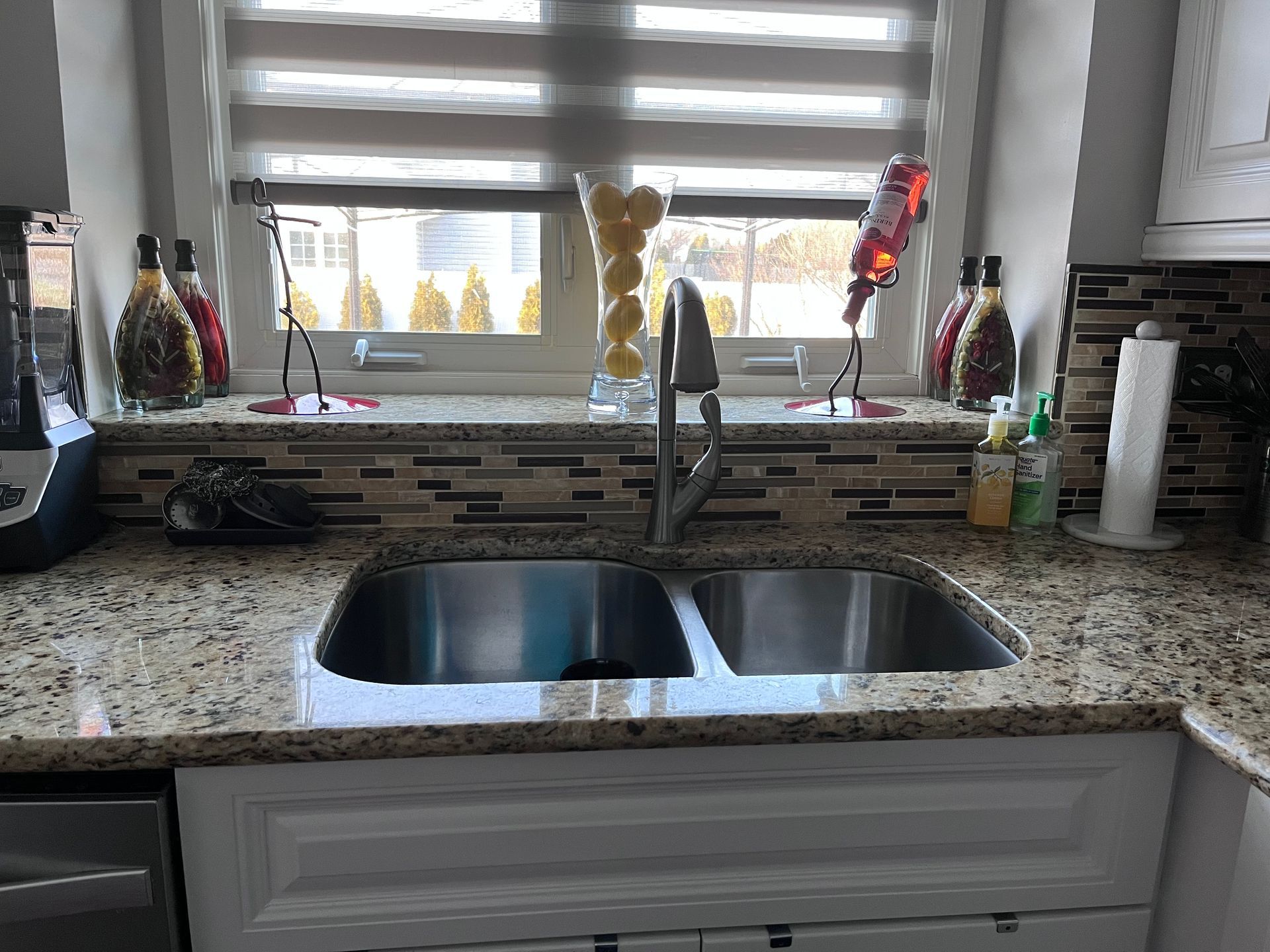 Kitchen sink under window with granite countertop, mosaic backsplash, and soap dispenser