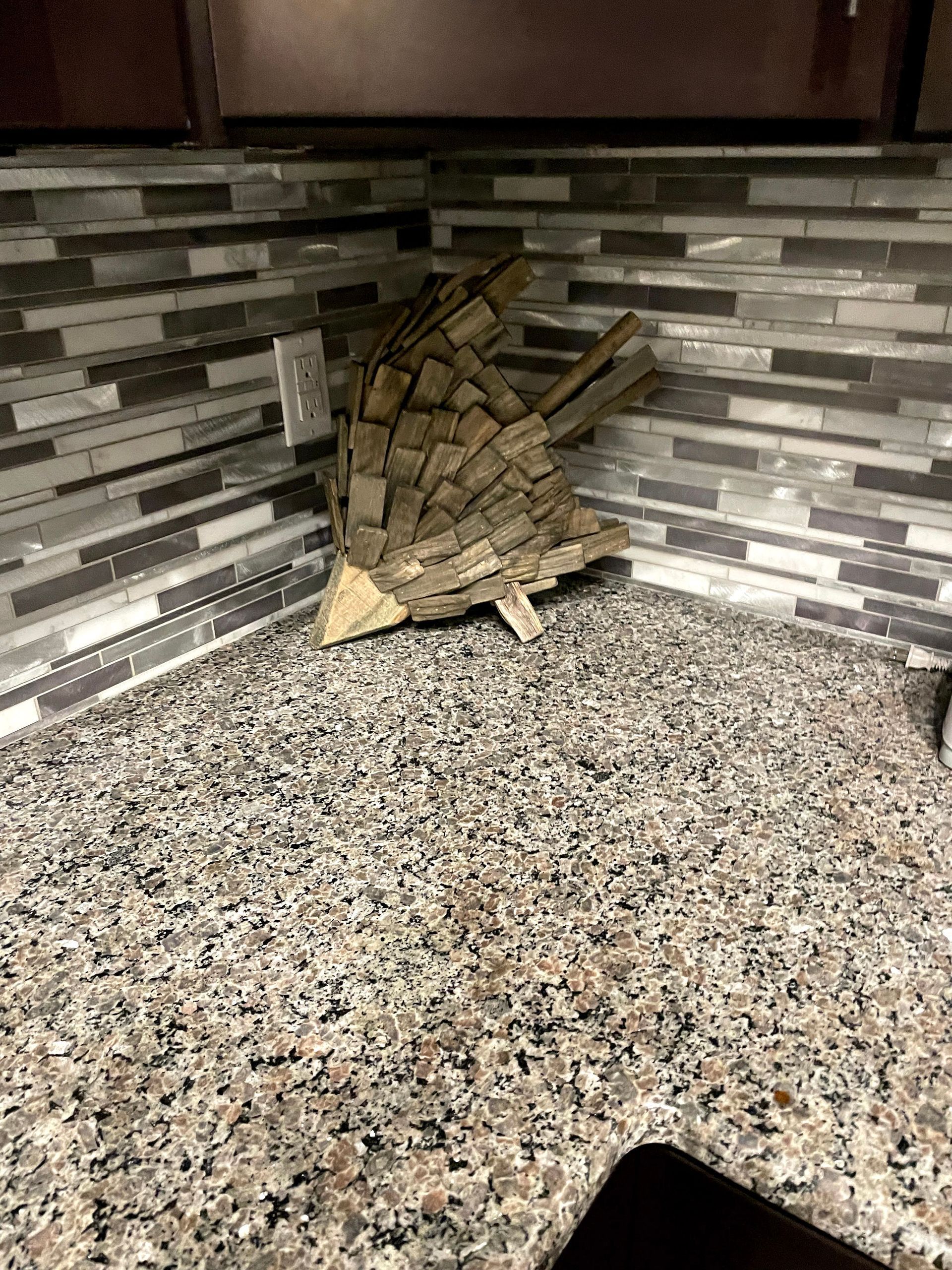Kitchen corner with gray tile backsplash and speckled countertop, showing a decorative stone sculpture.
