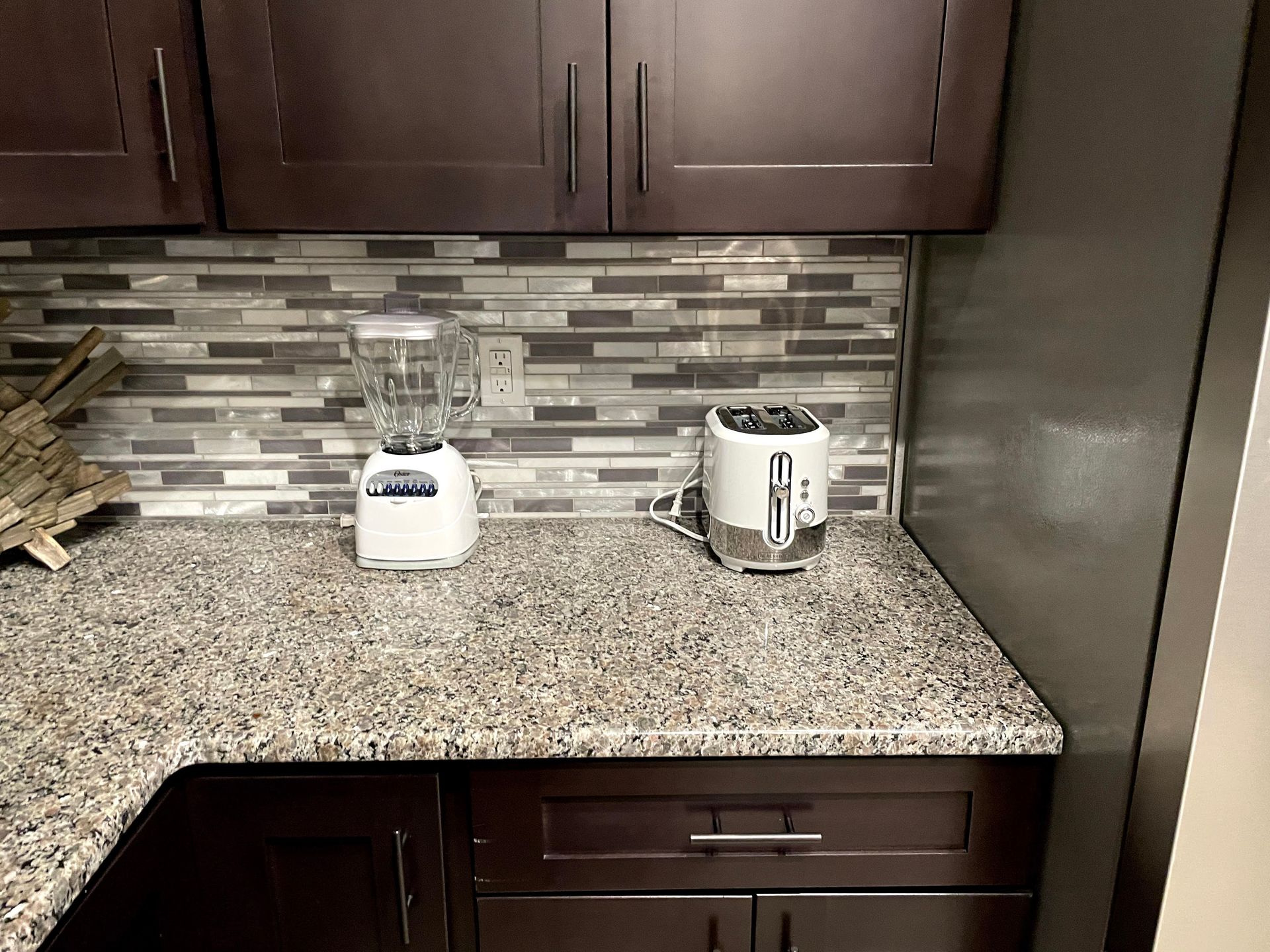 Kitchen counter with a white blender and toaster on a granite countertop under dark cabinets.