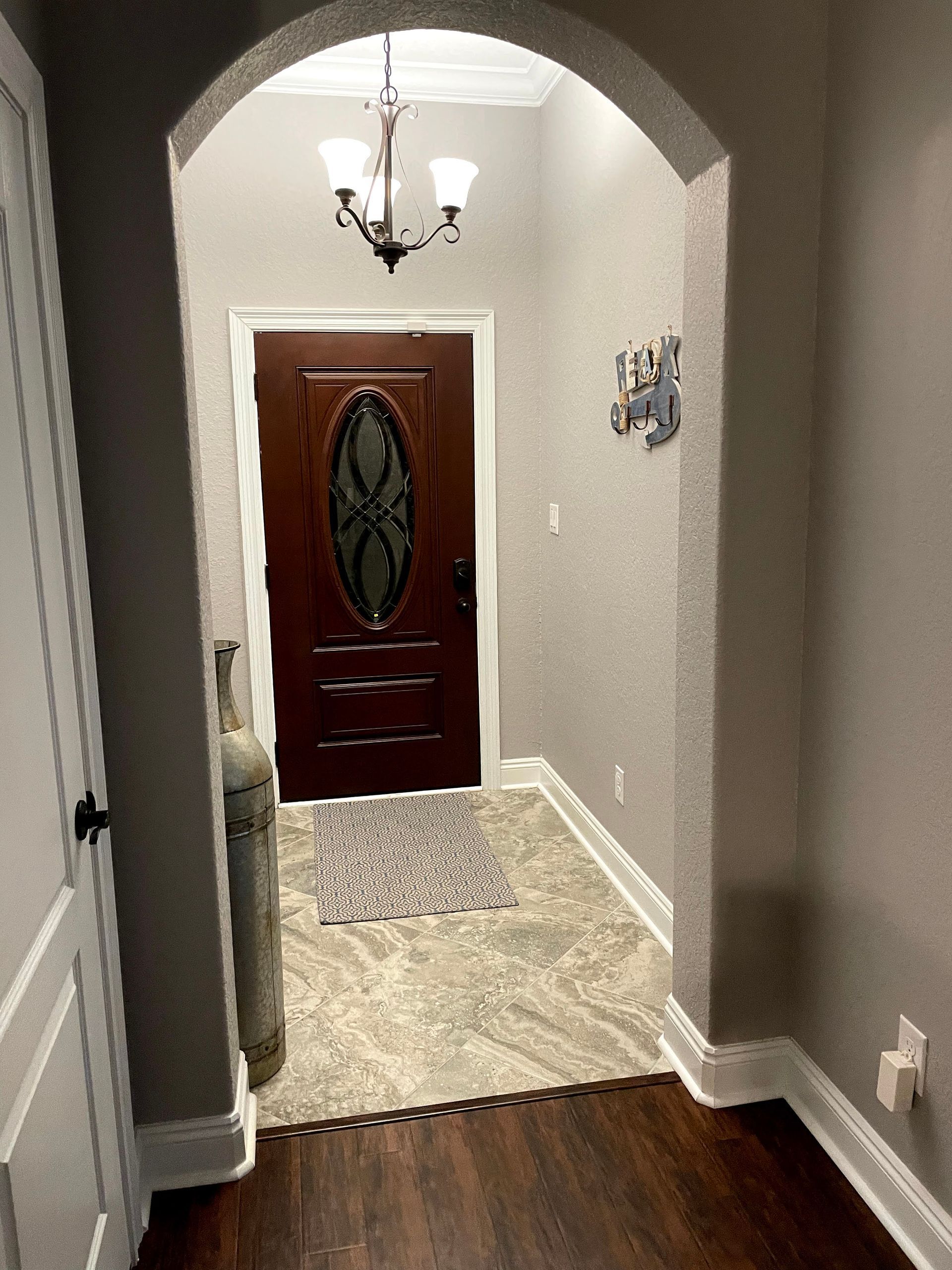 Hallway with arched ceiling, patterned runner rug, chandelier, and a wooden front door at the end.