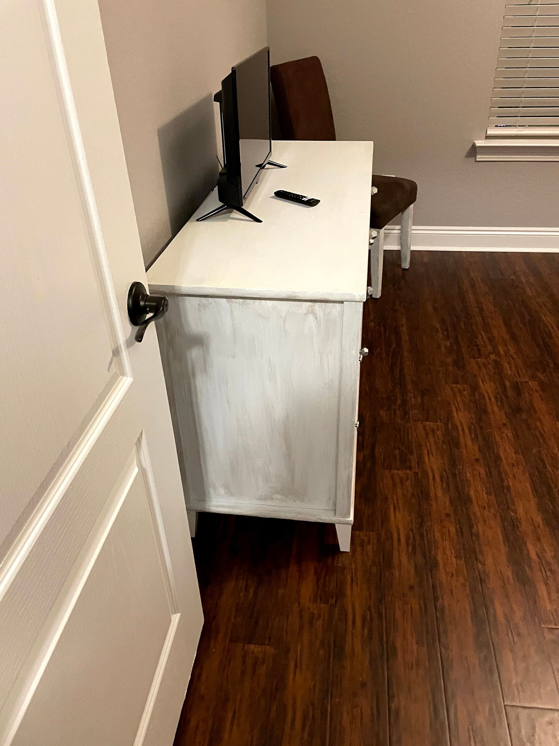 Small TV on a white-covered dresser in a room with hardwood floor and a window blind.