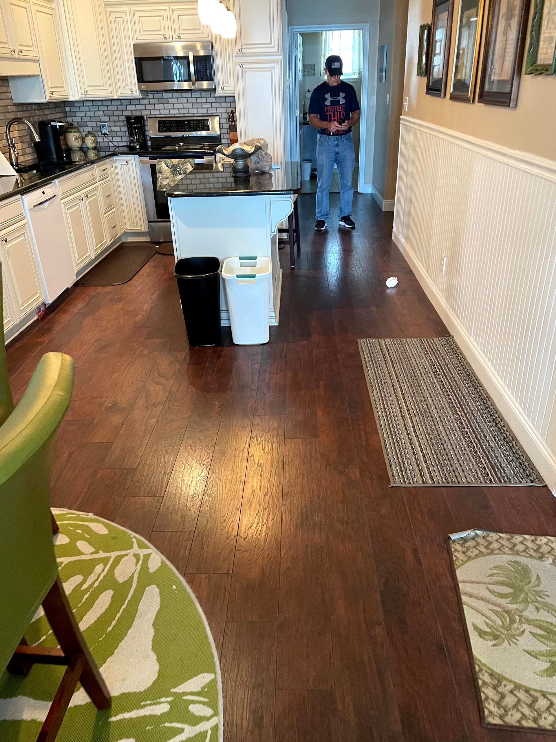 Long kitchen with patterned wallpaper, dark wood floor, and a person standing near the far counter.