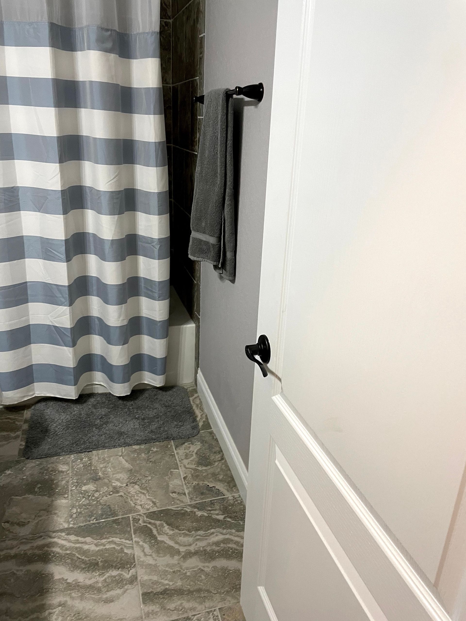 Bathroom or closet door partly open beside striped curtain and towel rack, with gray carpeted floor.