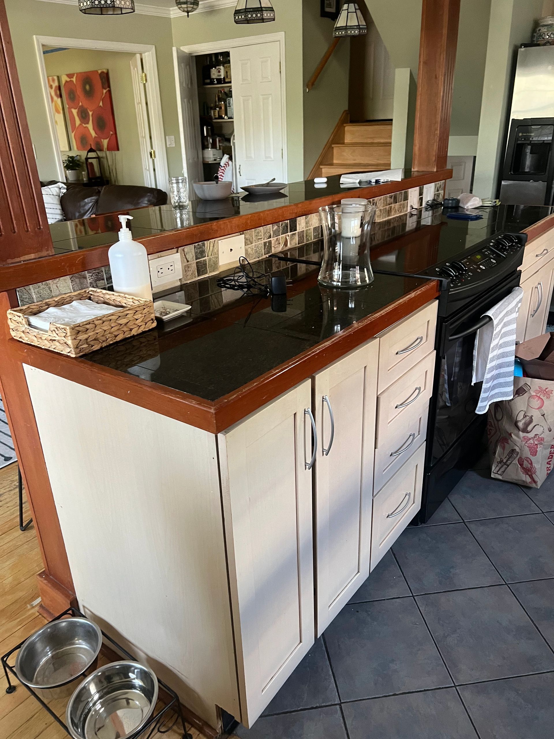 Kitchen island with dark countertop, white cabinets, sink, dish rack, and dog bowls on the floor