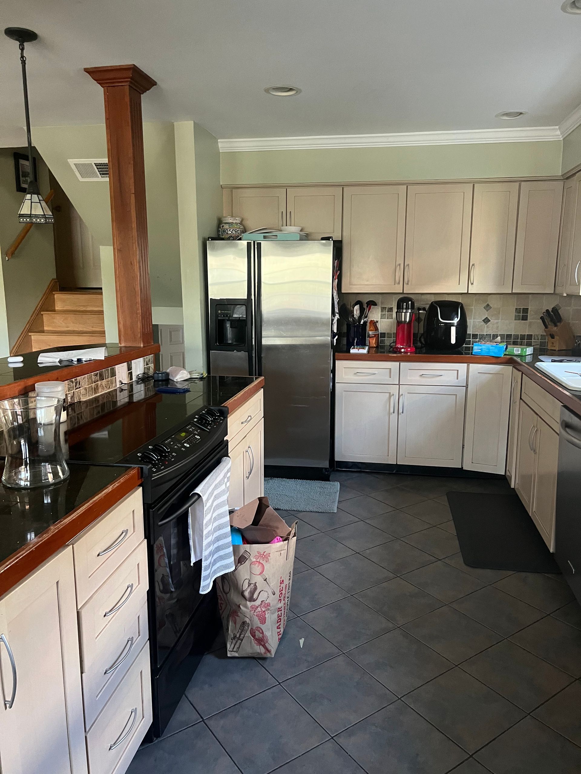 Kitchen with white cabinets, stainless fridge, dark countertops, and tiled floor.