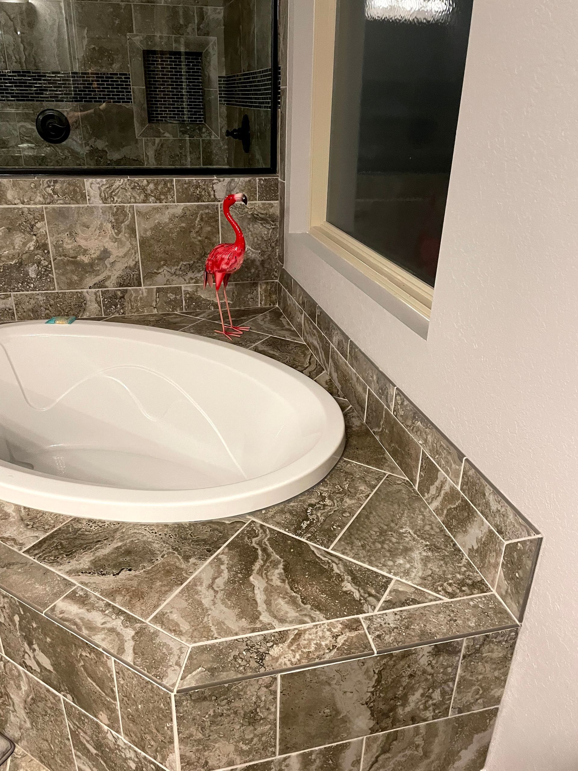 Bathroom sink with white basin, brown stone countertop, and a red faucet beside a window.