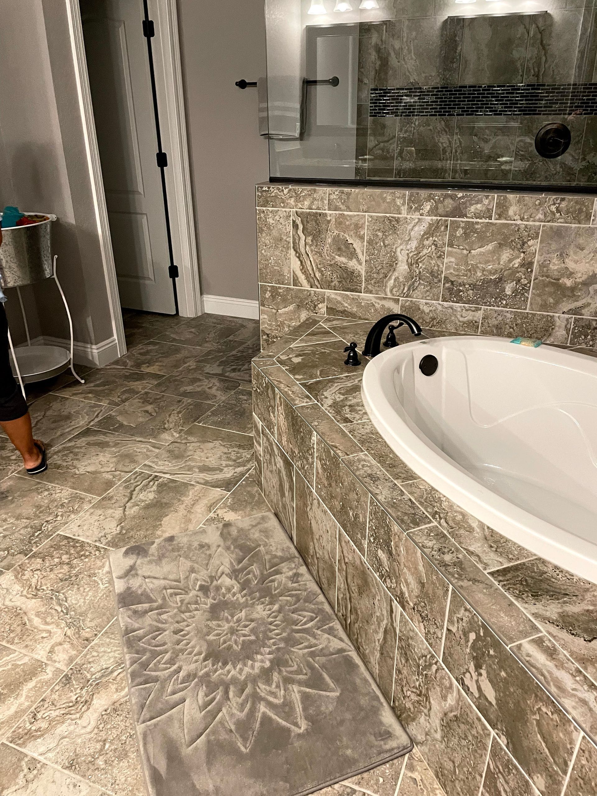 Marble bathroom with a corner tub, stone vanity, and tiled floor; door and mirror visible.
