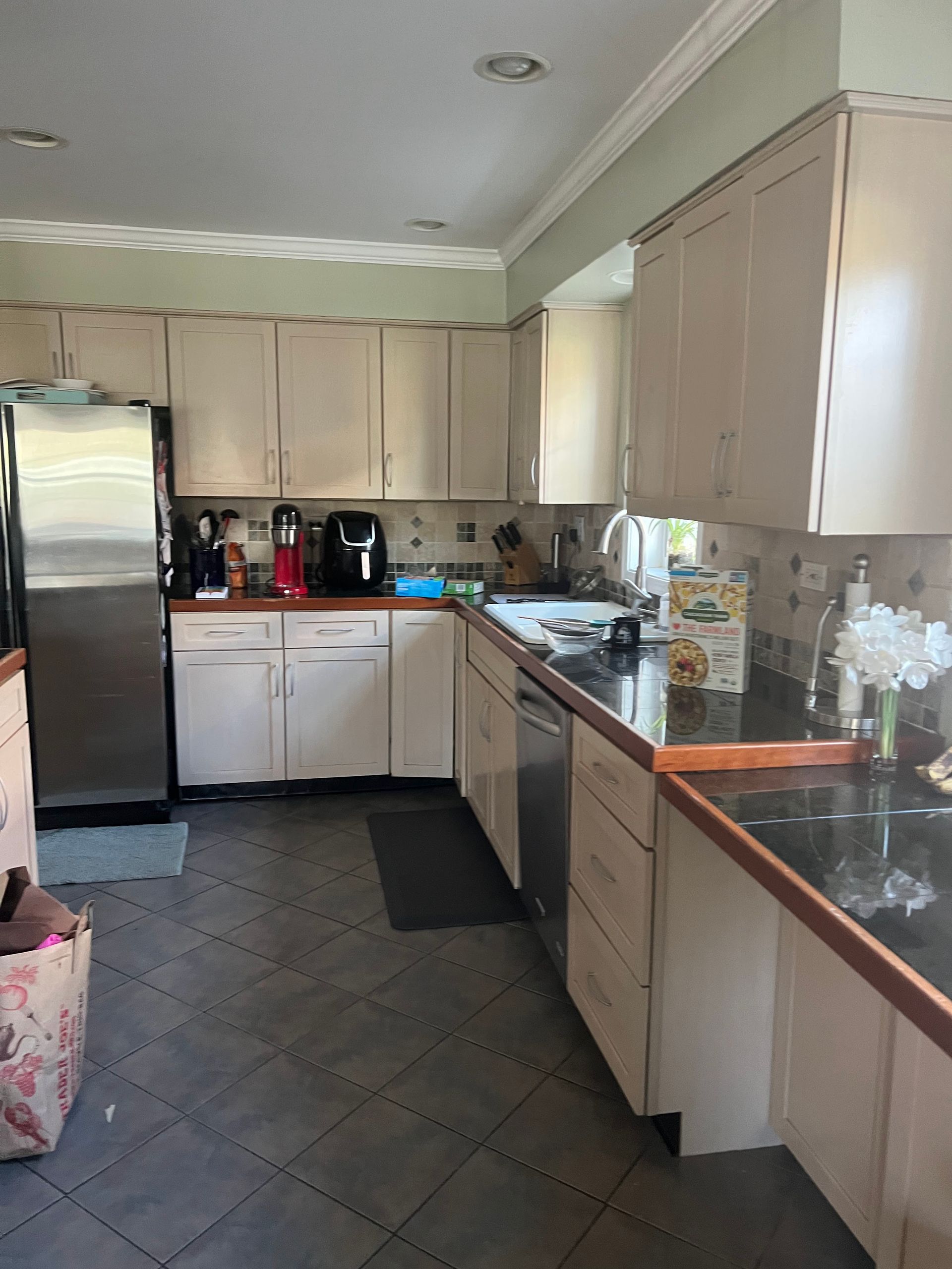 Bright kitchen with beige cabinets, stainless fridge, dark tile floor, and coffee maker on the counter.