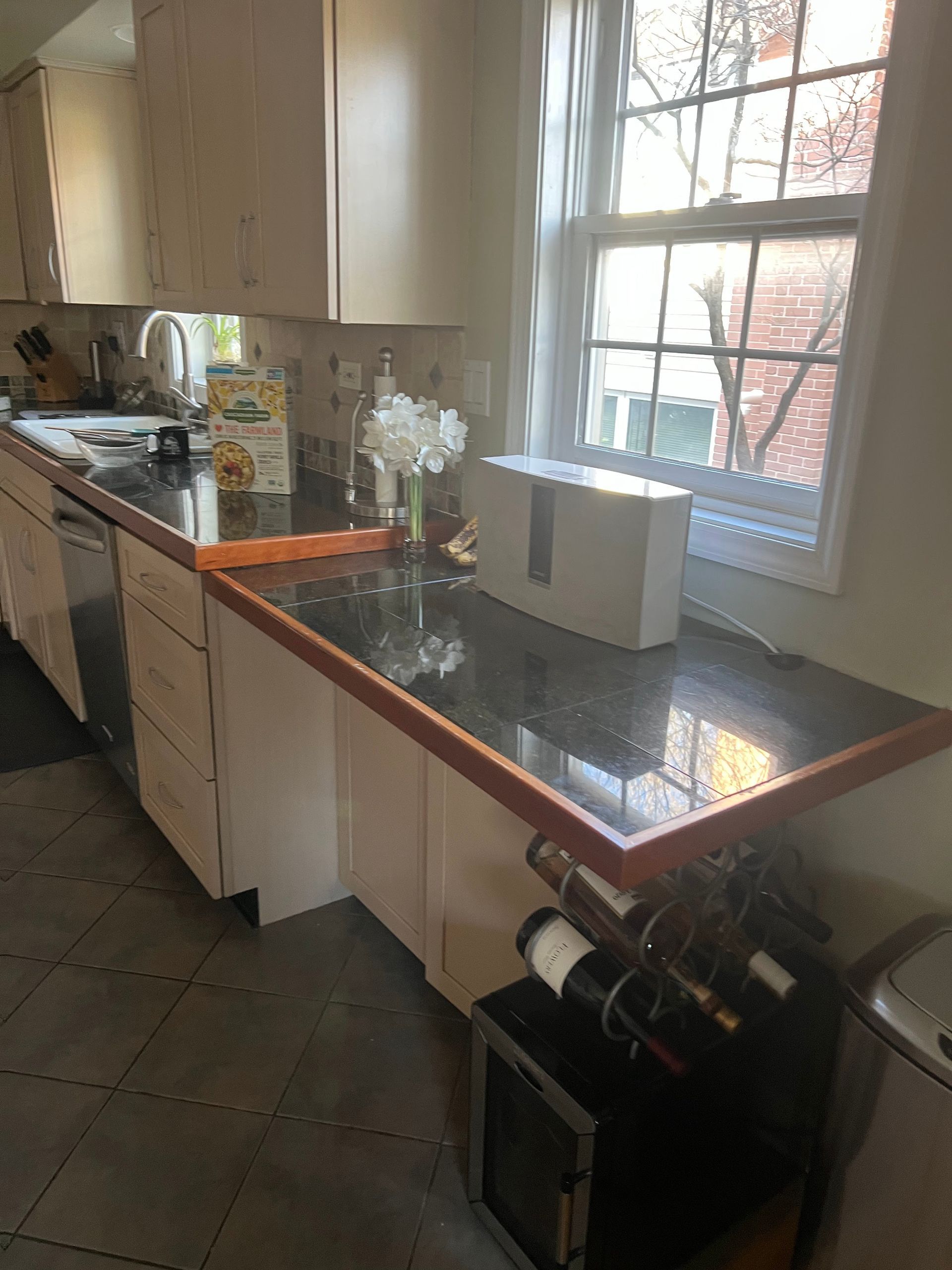Kitchen counter by window with granite top, wine rack below, and white cabinets in a sunlit room
