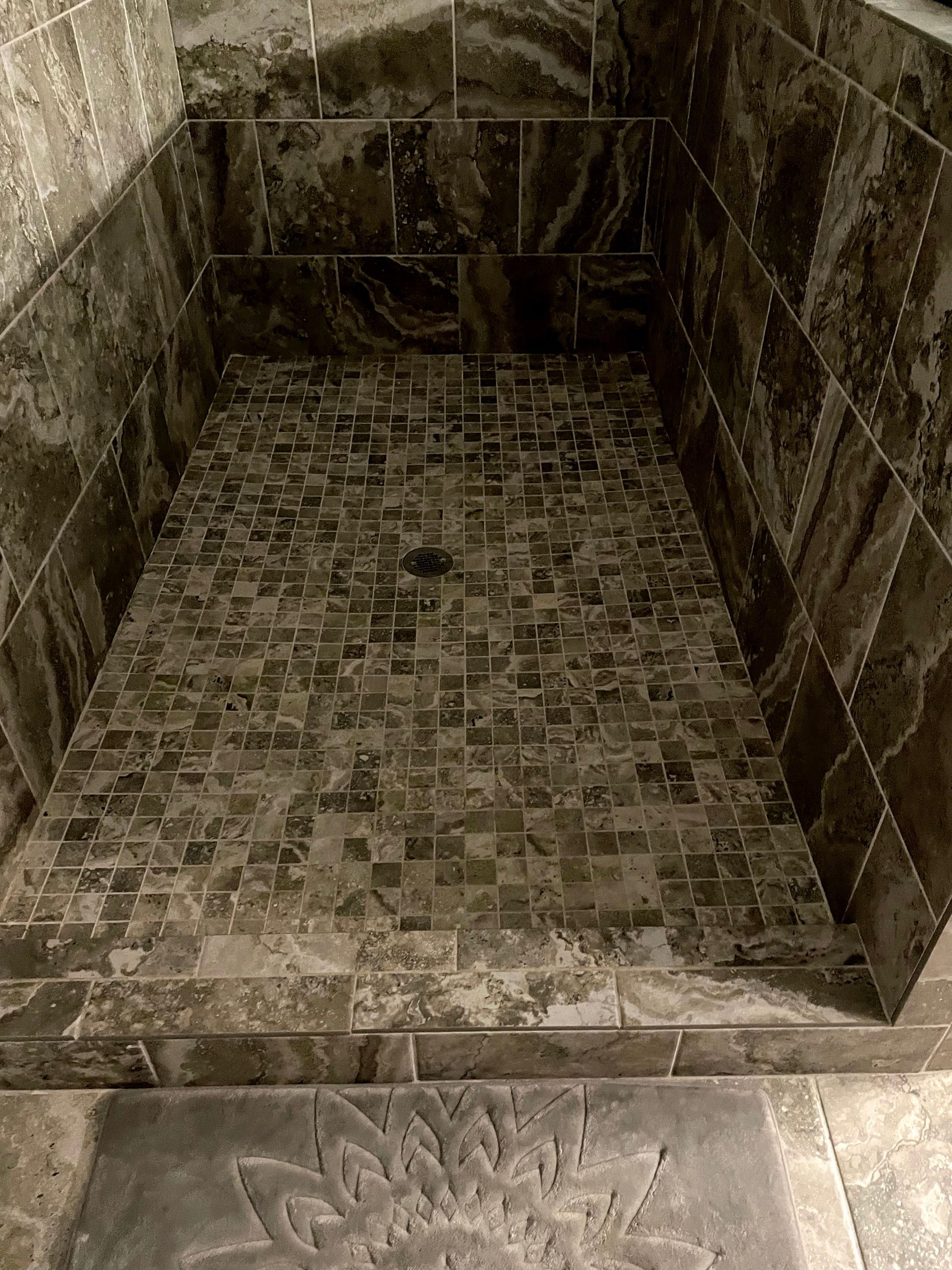 Empty tiled shower stall with stone walls and floor, viewed from the entrance.