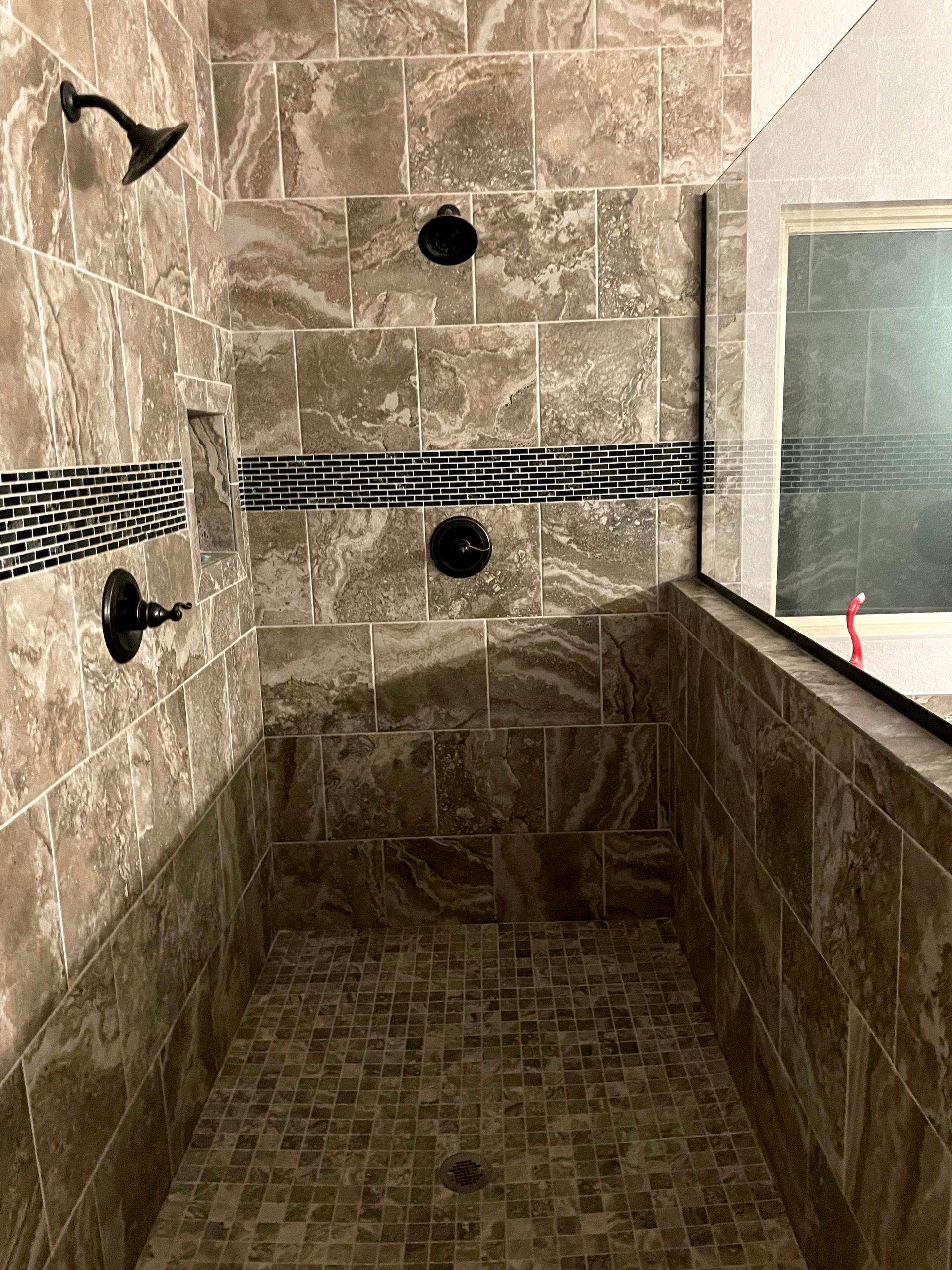 Empty tiled shower with black fixtures and a glass window.