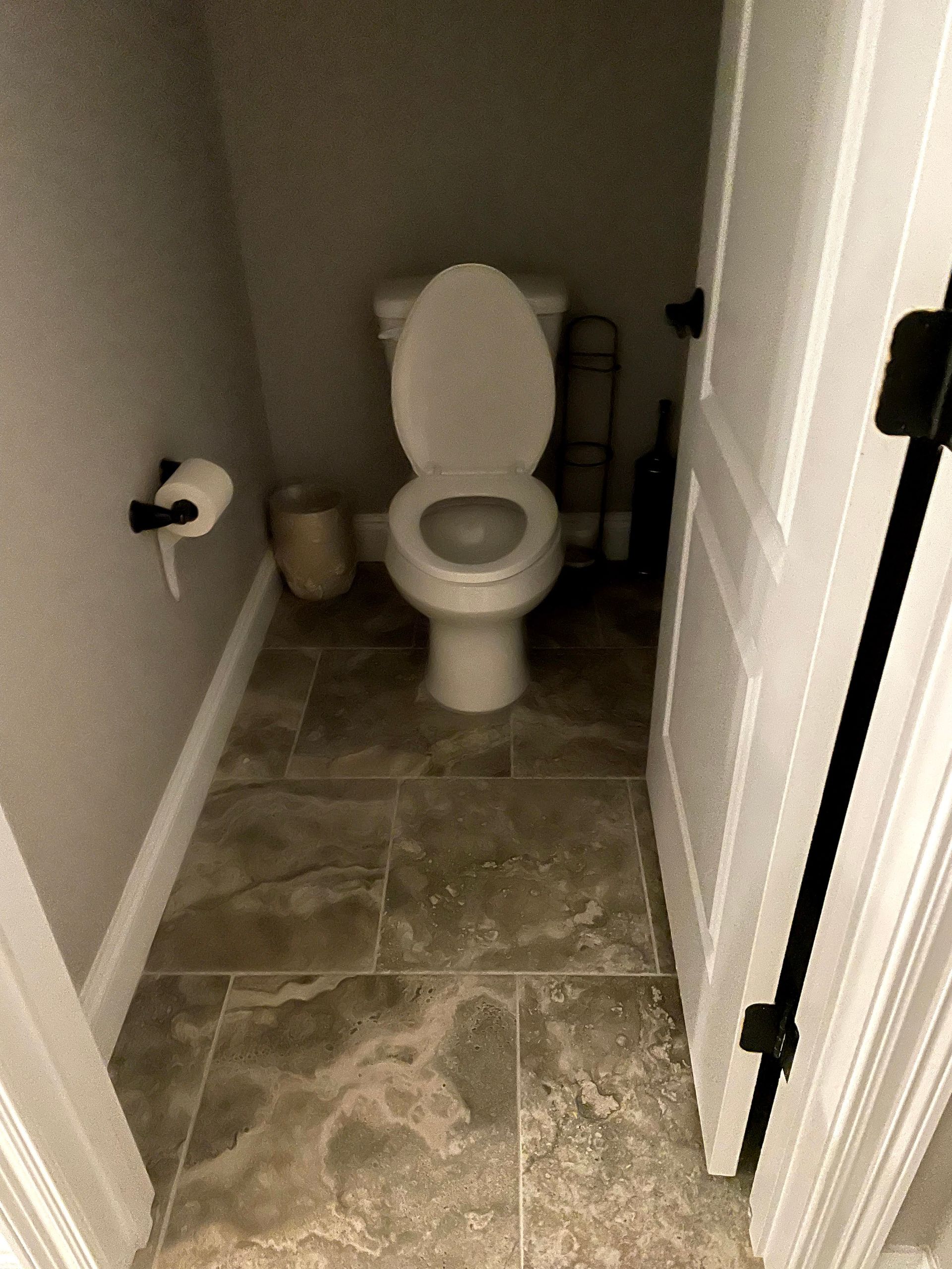 Small bathroom with a white toilet, tiled floor, and a toilet paper holder on the left wall.