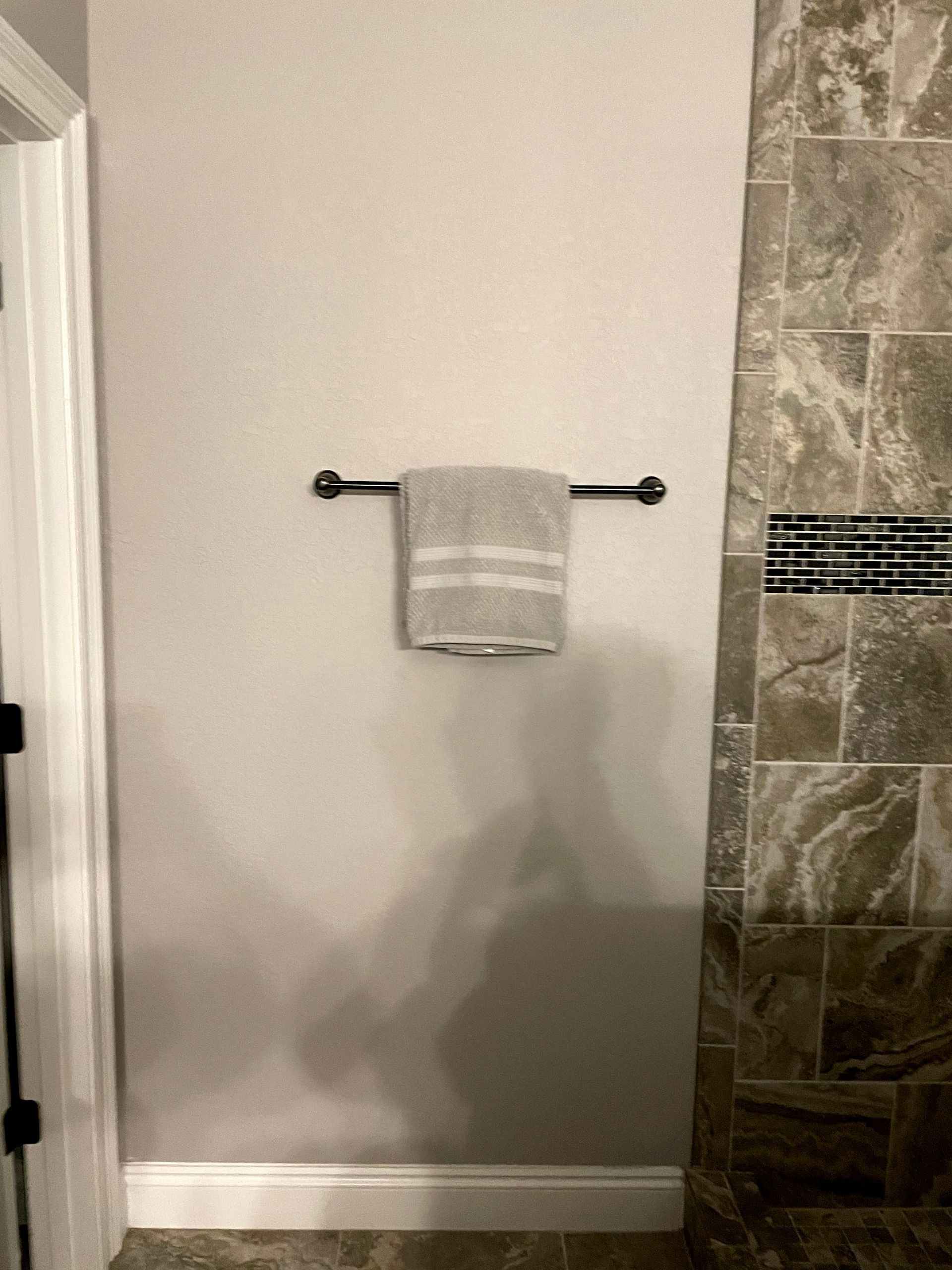 Towel bar with a folded gray towel on a light wall beside a stone-tiled shower wall.
