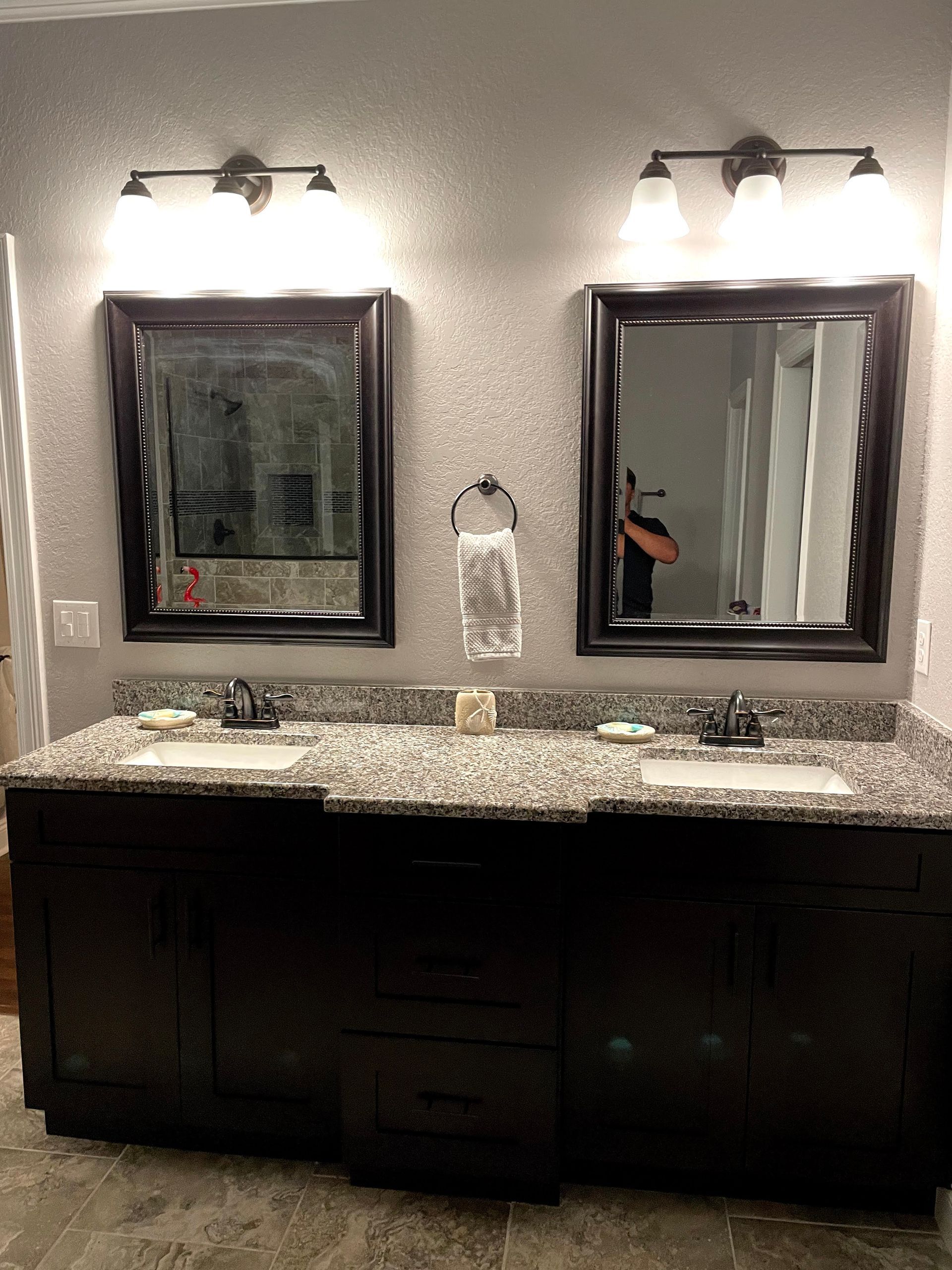 Double bathroom vanity with two lit mirrors, granite countertop, and dark cabinets.