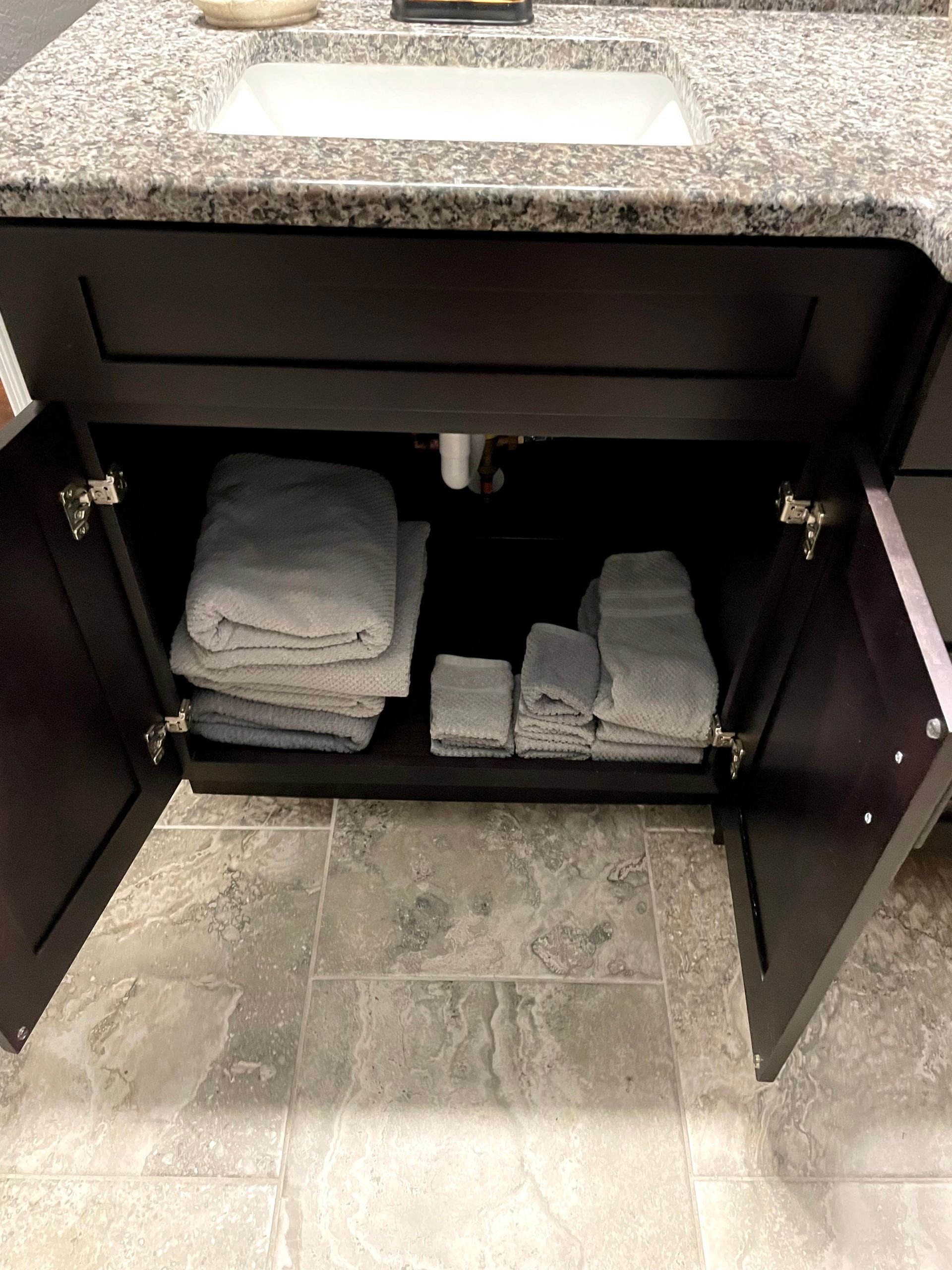 Open bathroom vanity cabinet with folded gray towels on the shelves.