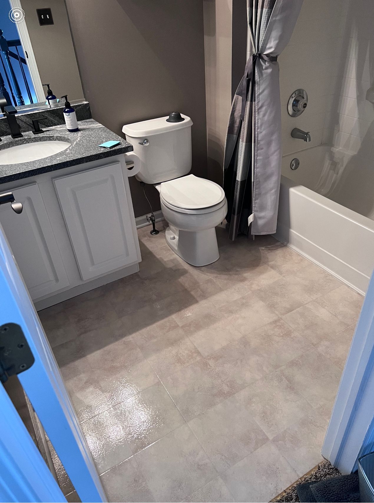 Small bathroom with gray tile floor, vanity, toilet, shower curtain, and bathtub.