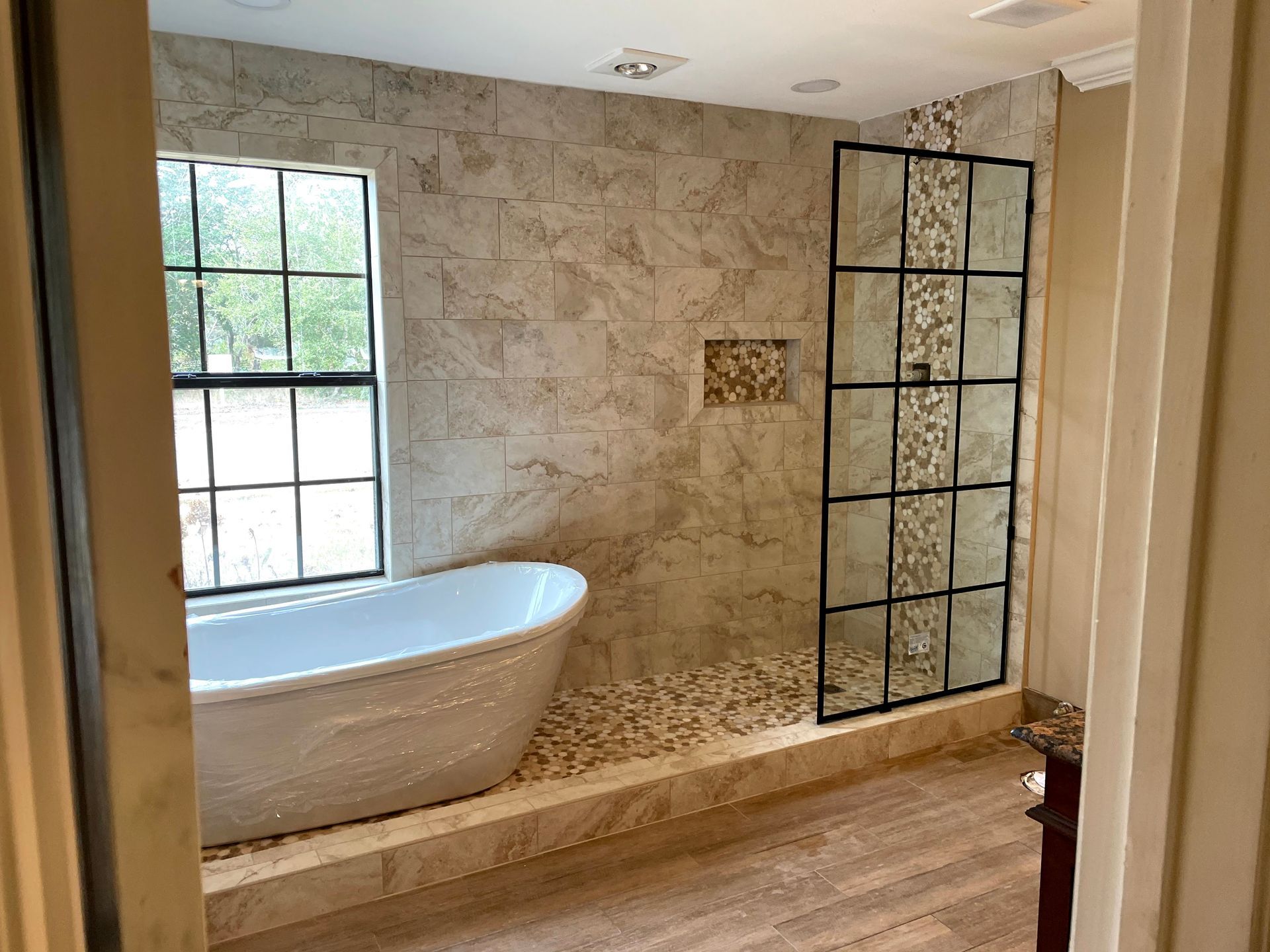 Bathroom with freestanding tub, stone walls, black-framed window, and glass shower enclosure.