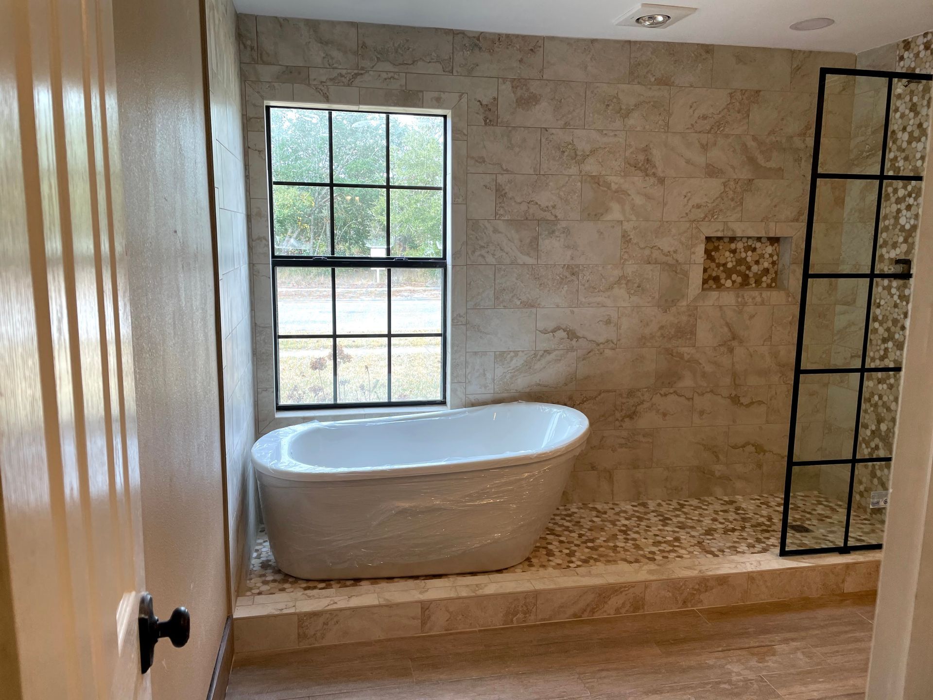 Bright bathroom with a freestanding bathtub, tiled shower area, and window.
