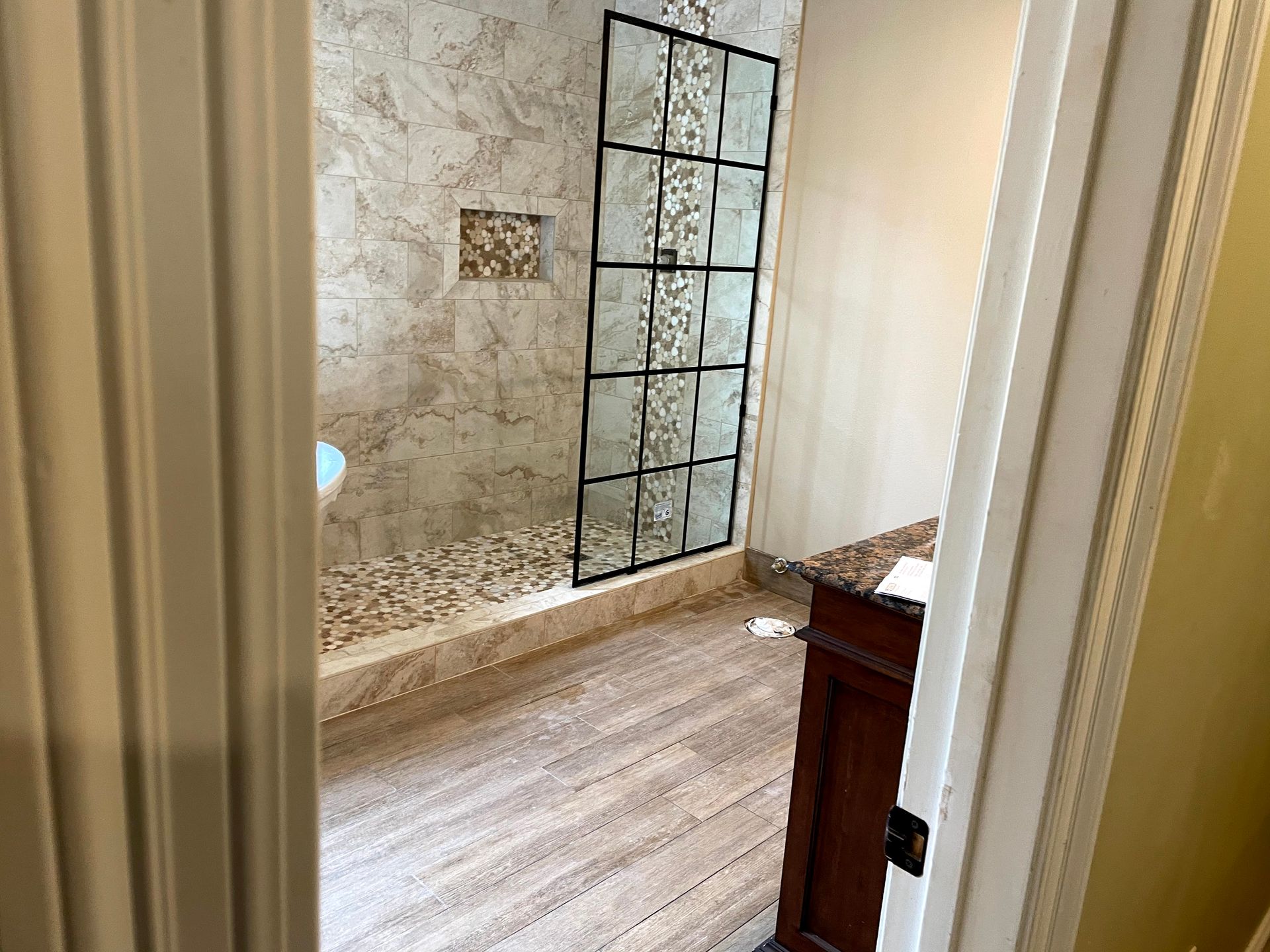 Stone bathroom with glass shower wall and beige floor seen through an open door