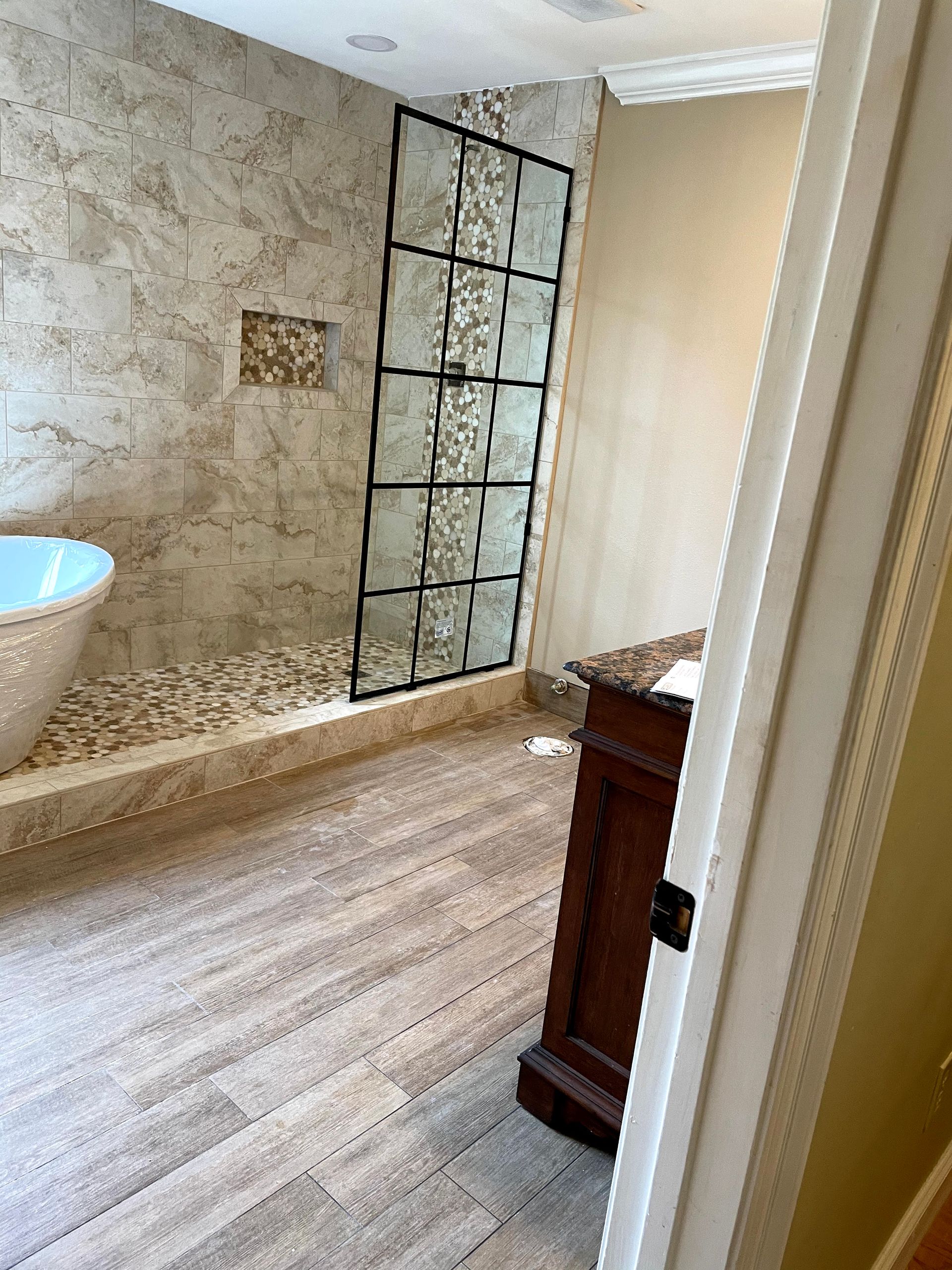 Luxury bathroom with stone walls, glass shower panel, and bathtub