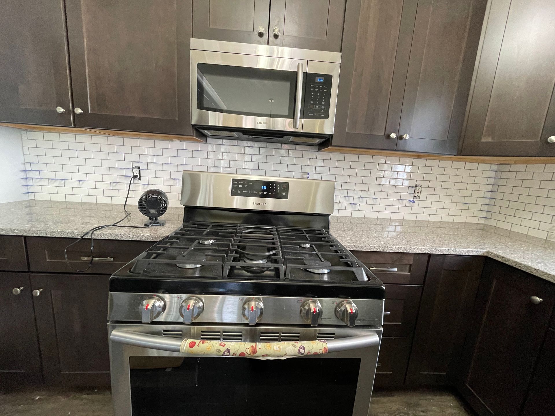 Modern kitchen with dark cabinets, stainless steel stove and microwave, and white tile backsplash.