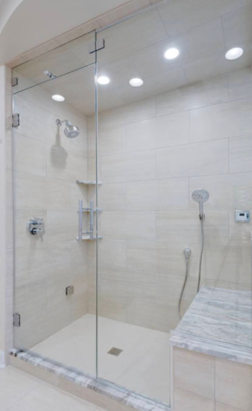 Modern beige tiled walk-in shower with glass door, built-in bench, and rain showerhead