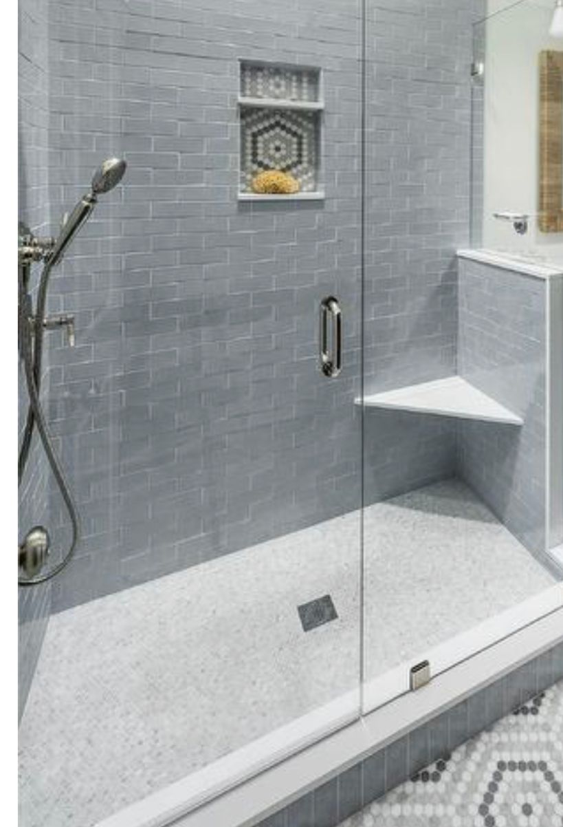 Gray-tiled walk-in shower with glass door, handheld showerhead, built-in shelf, and small corner bench.