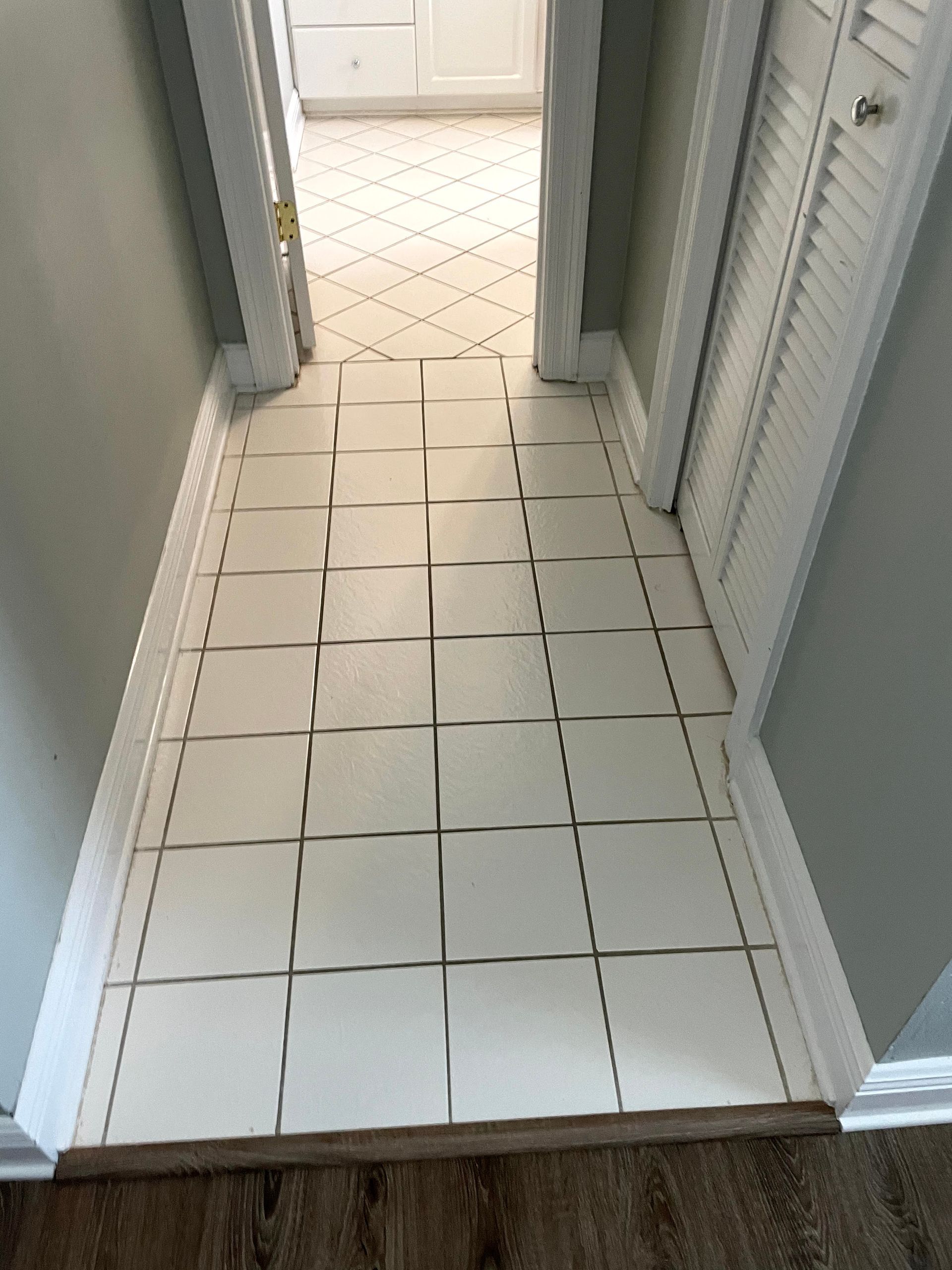 White tiled hallway floor leading to a doorway, with light gray walls and door trim.
