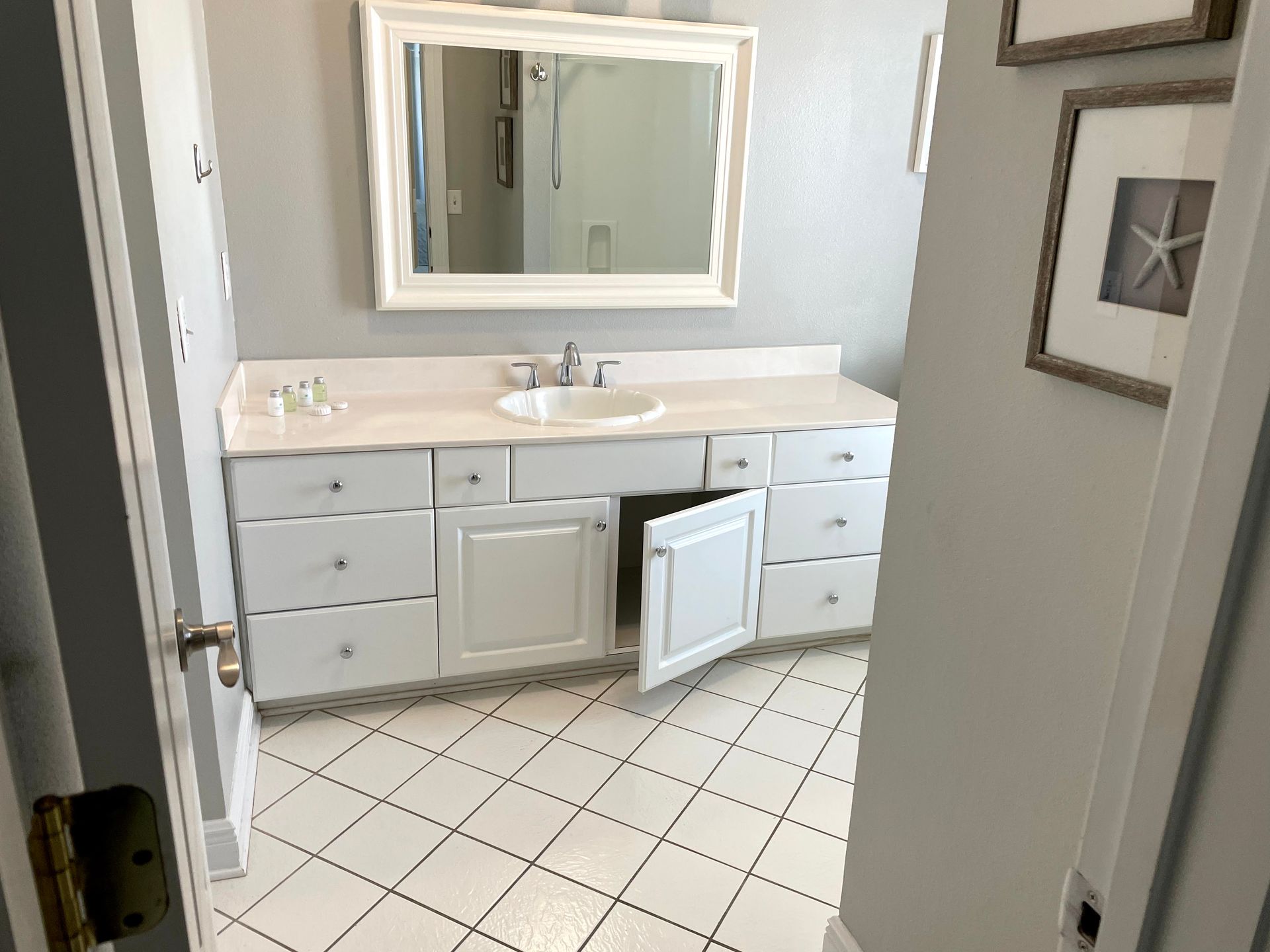 Bathroom with white vanity, mirror, and tiled floor; under-sink cabinet door is open.