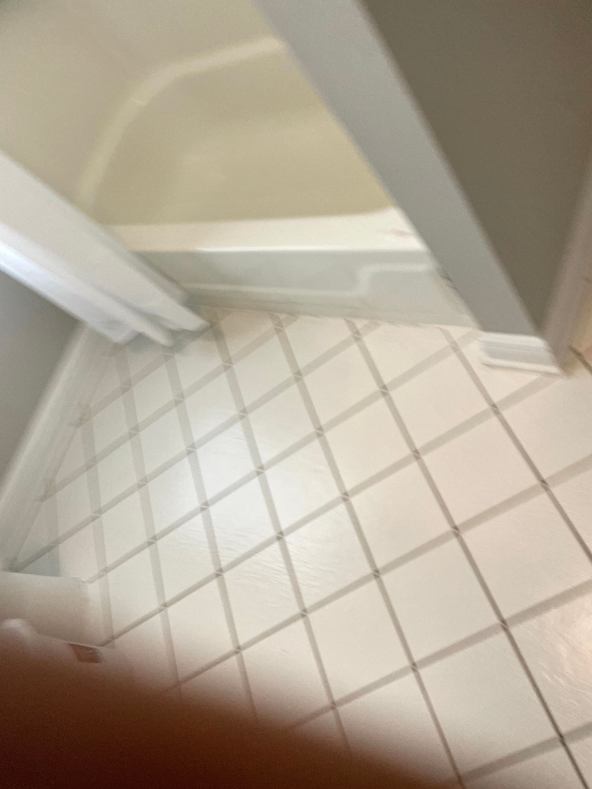 Tiled bathroom floor beside a shower curtain and beige wall, with a finger partially covering the lens