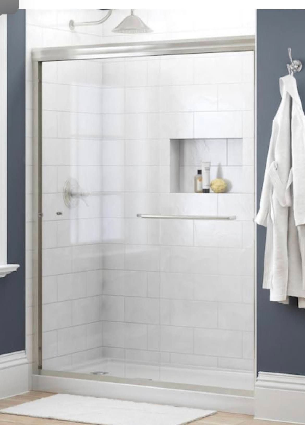 White tiled walk-in shower with glass door, built-in shelf, and hanging robe in a bathroom