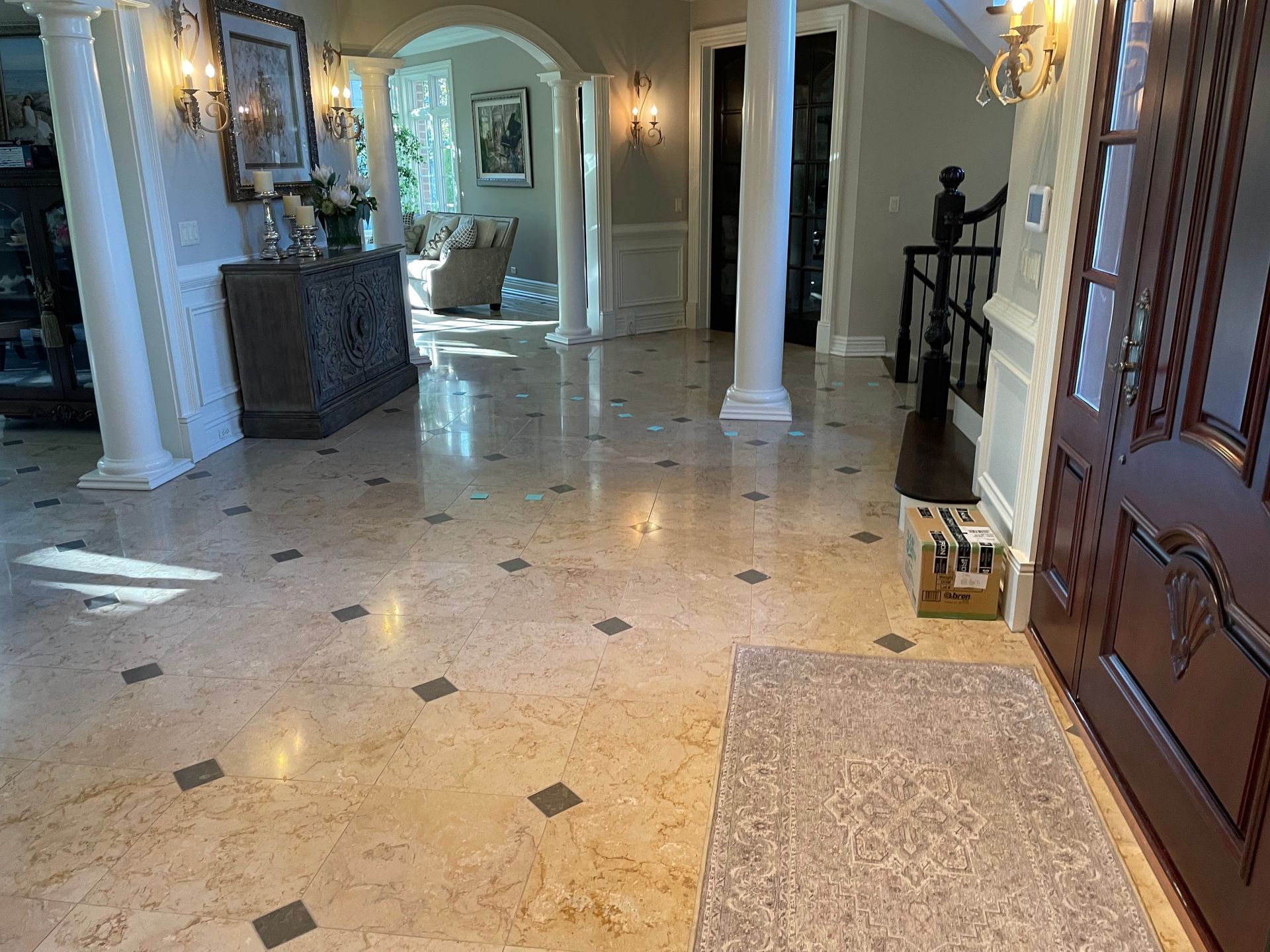Elegant foyer with marble floors, white columns, a dark wooden door, and a rug by the entryway.