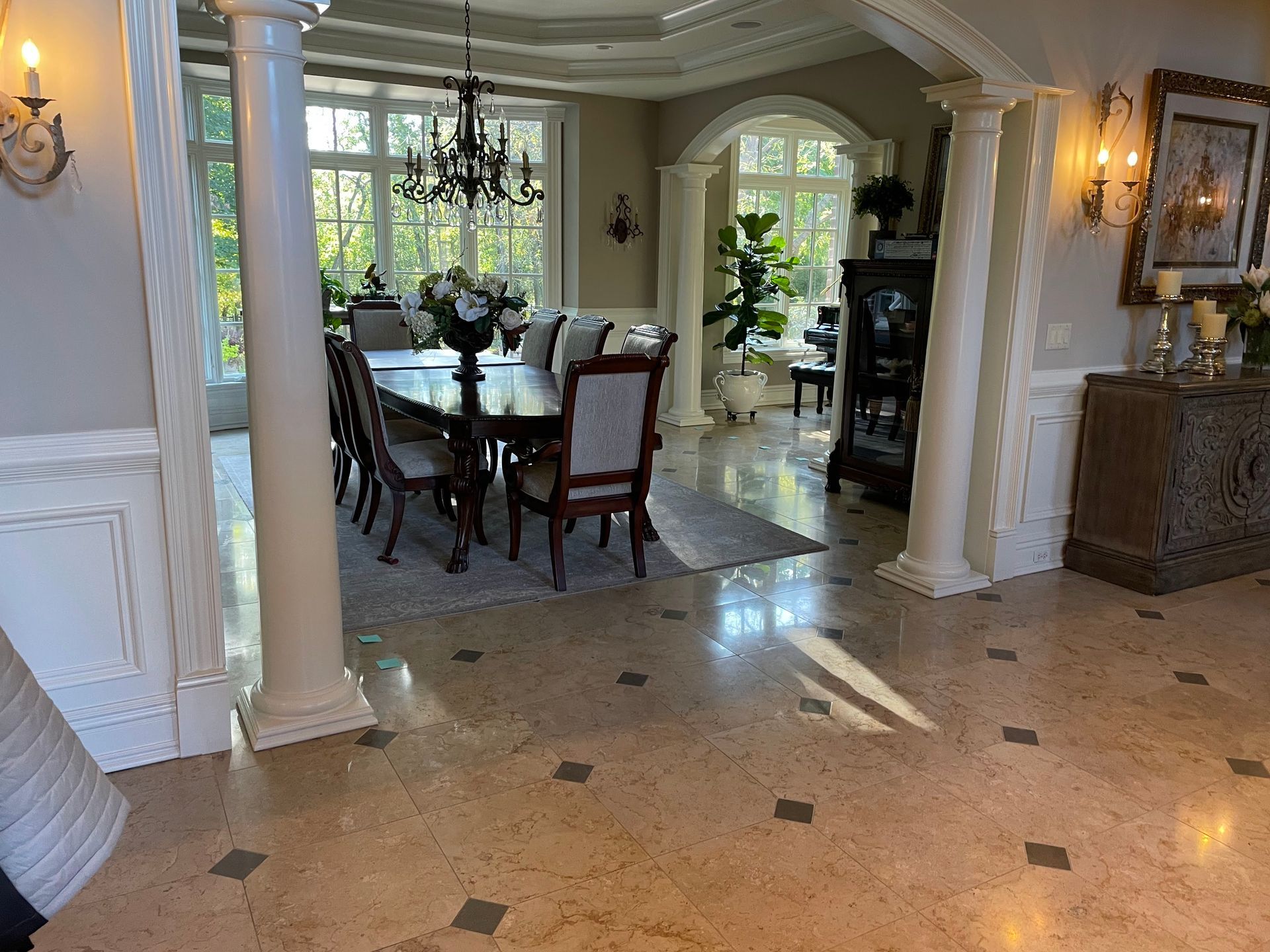 Elegant dining room and foyer with polished marble floor, dark wood table, chairs, and large windows overlooking greenery